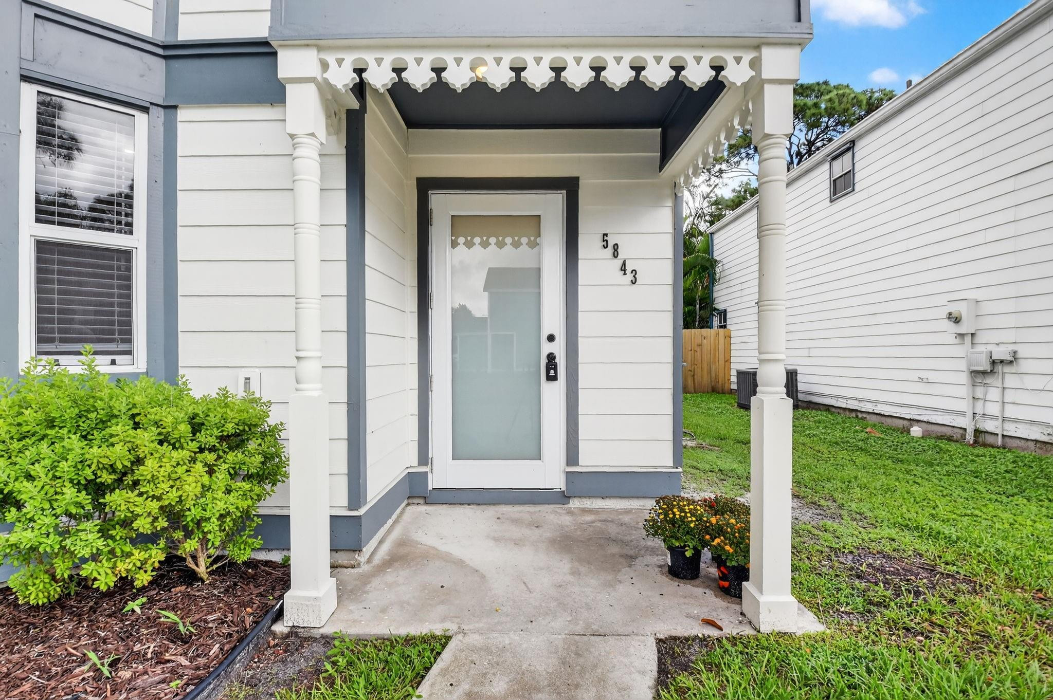 Home entrance with decorative white porch trim, blue-gray accents, and house number 5843.