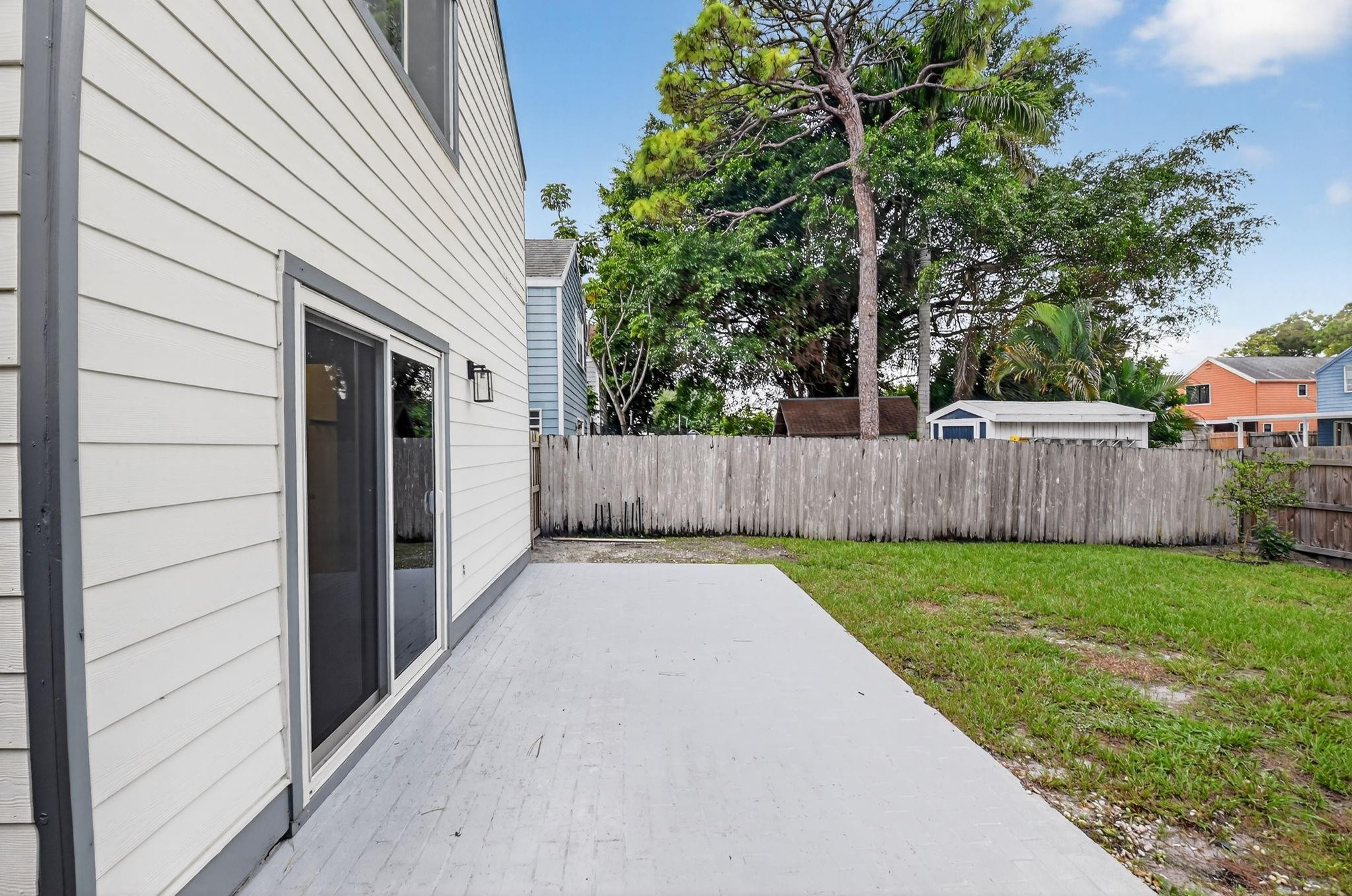 Concrete patio beside a white-sided home, overlooking a fenced lawn with mature trees.