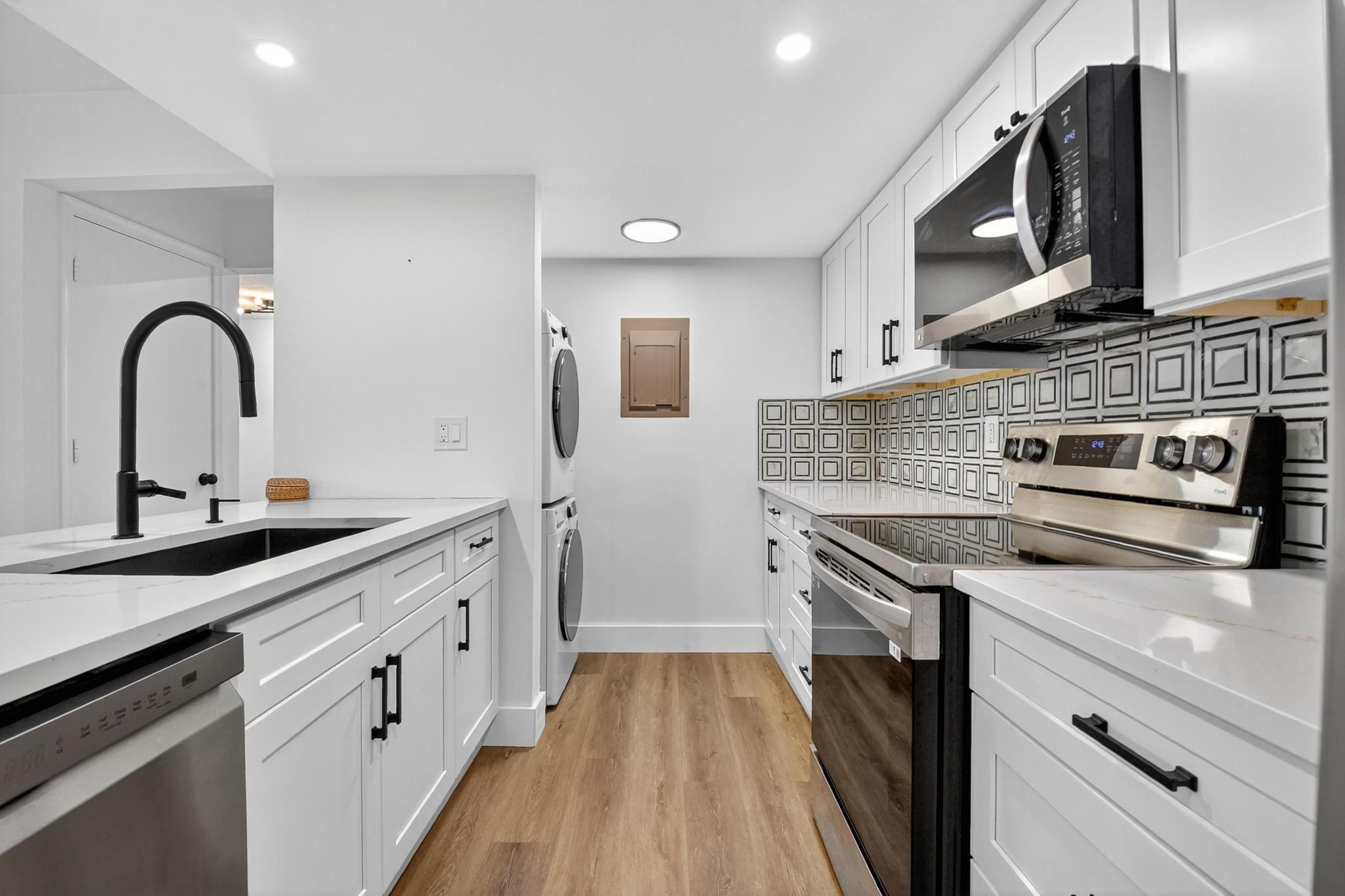 Galley kitchen with white cabinets, stainless steel appliances, geometric backsplash, and a stacked washer and dryer.
