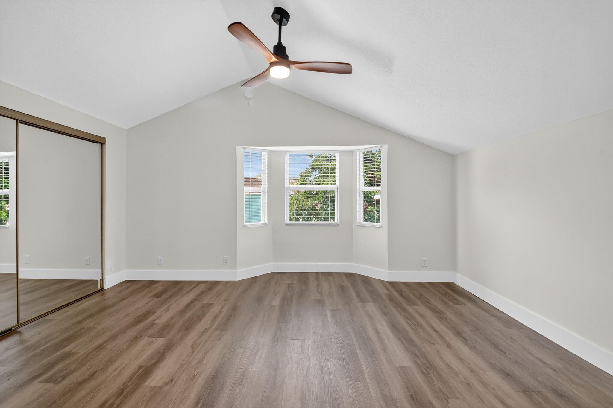 Empty bedroom with vaulted ceiling, mirrored closet doors, and a three-window bay.