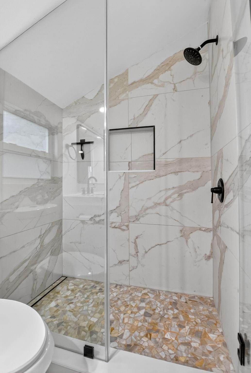 Walk-in shower with marble-look walls, a multicolor mosaic floor, and black fixtures.
