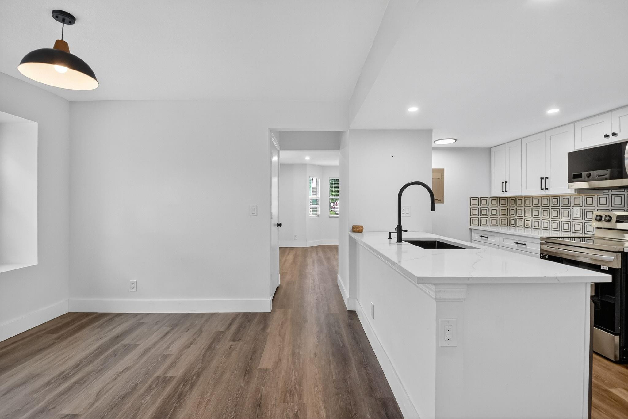 Modern kitchen with a large white island, black faucet, geometric backsplash, and stainless steel appliances.