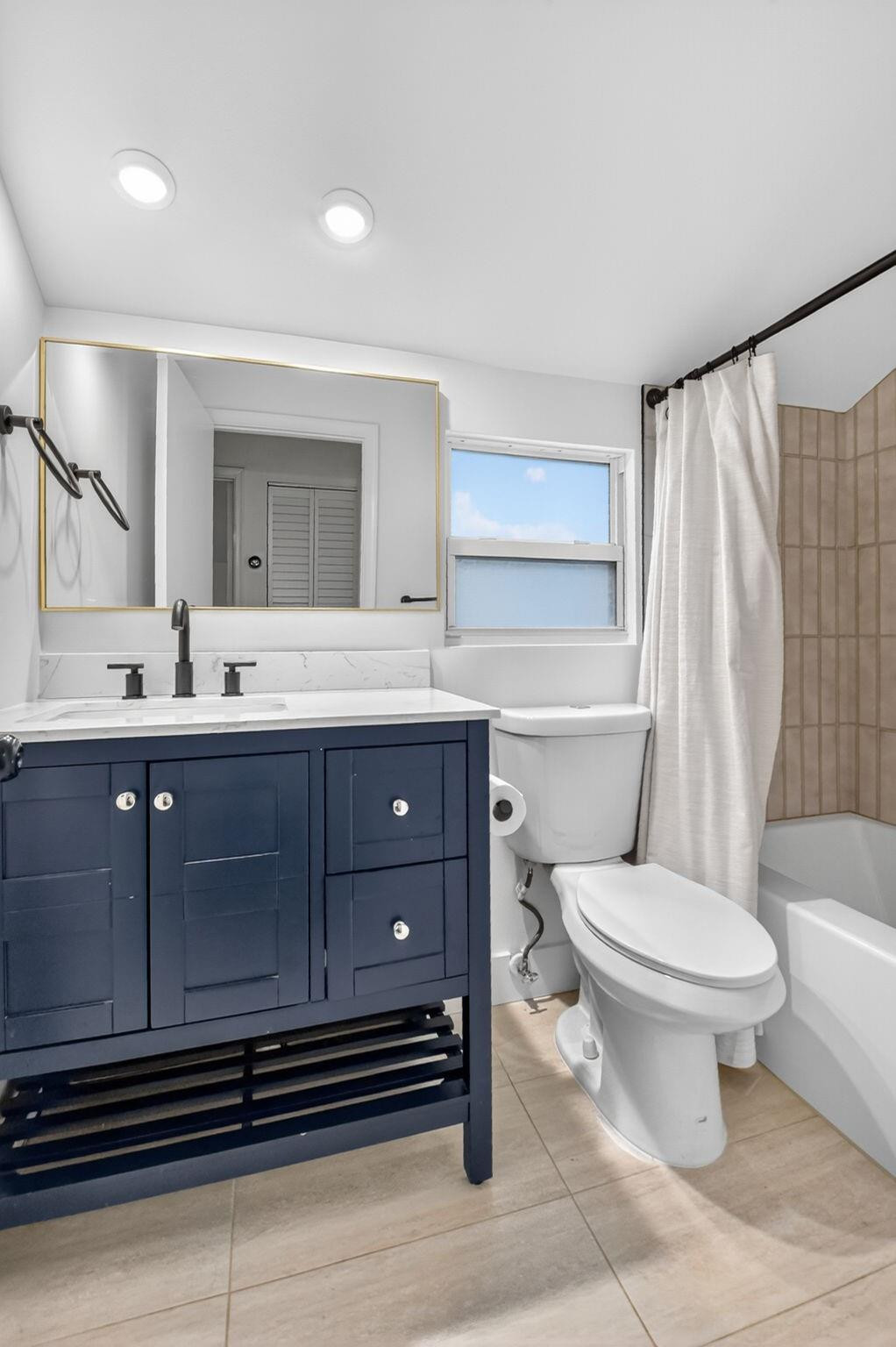 Bathroom with navy vanity, white countertop, toilet, and tub-shower with tiled surround.