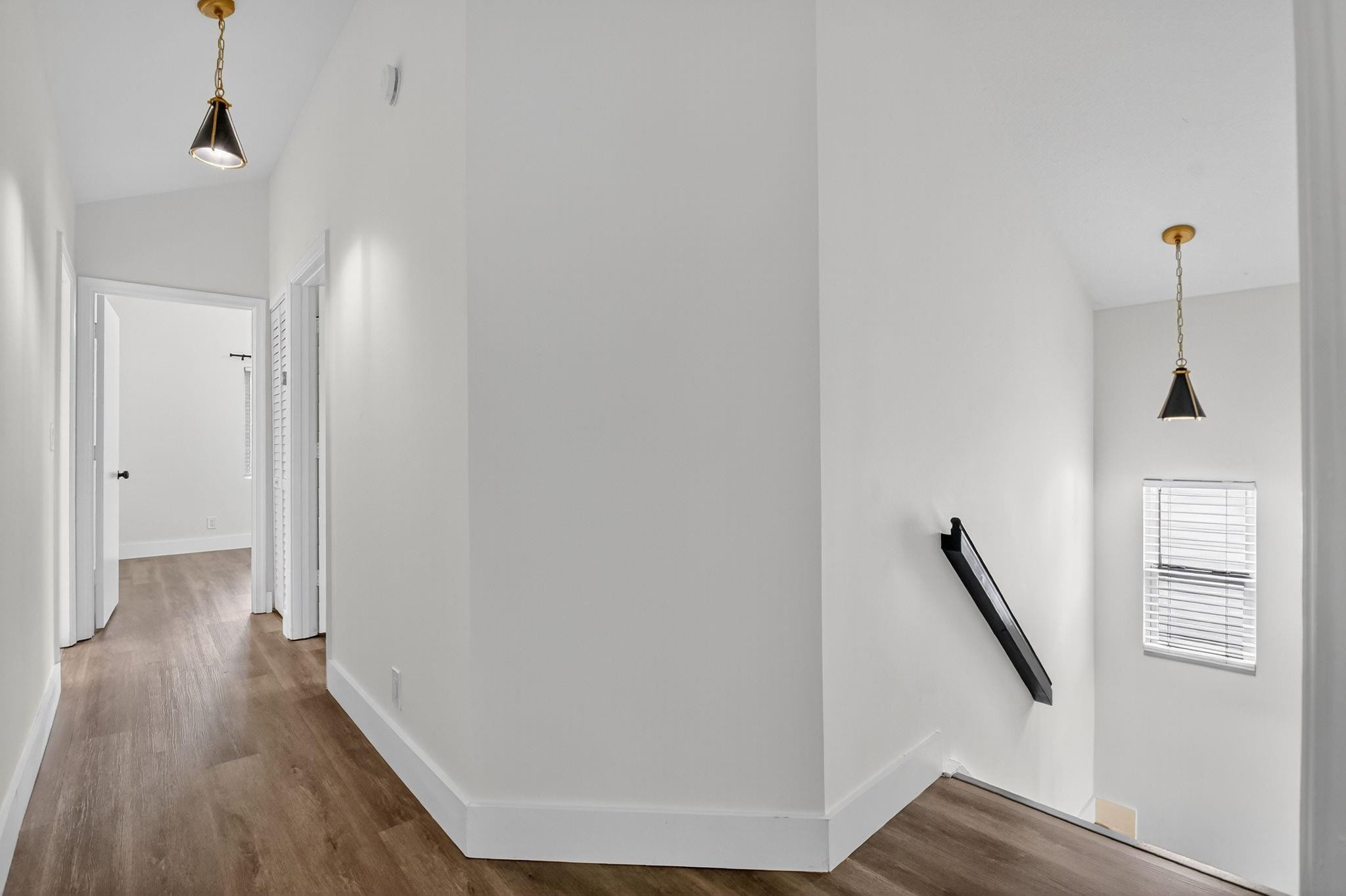 Vacant stair landing with brown wood-look floors, black pendant lights, and a window with white blinds.