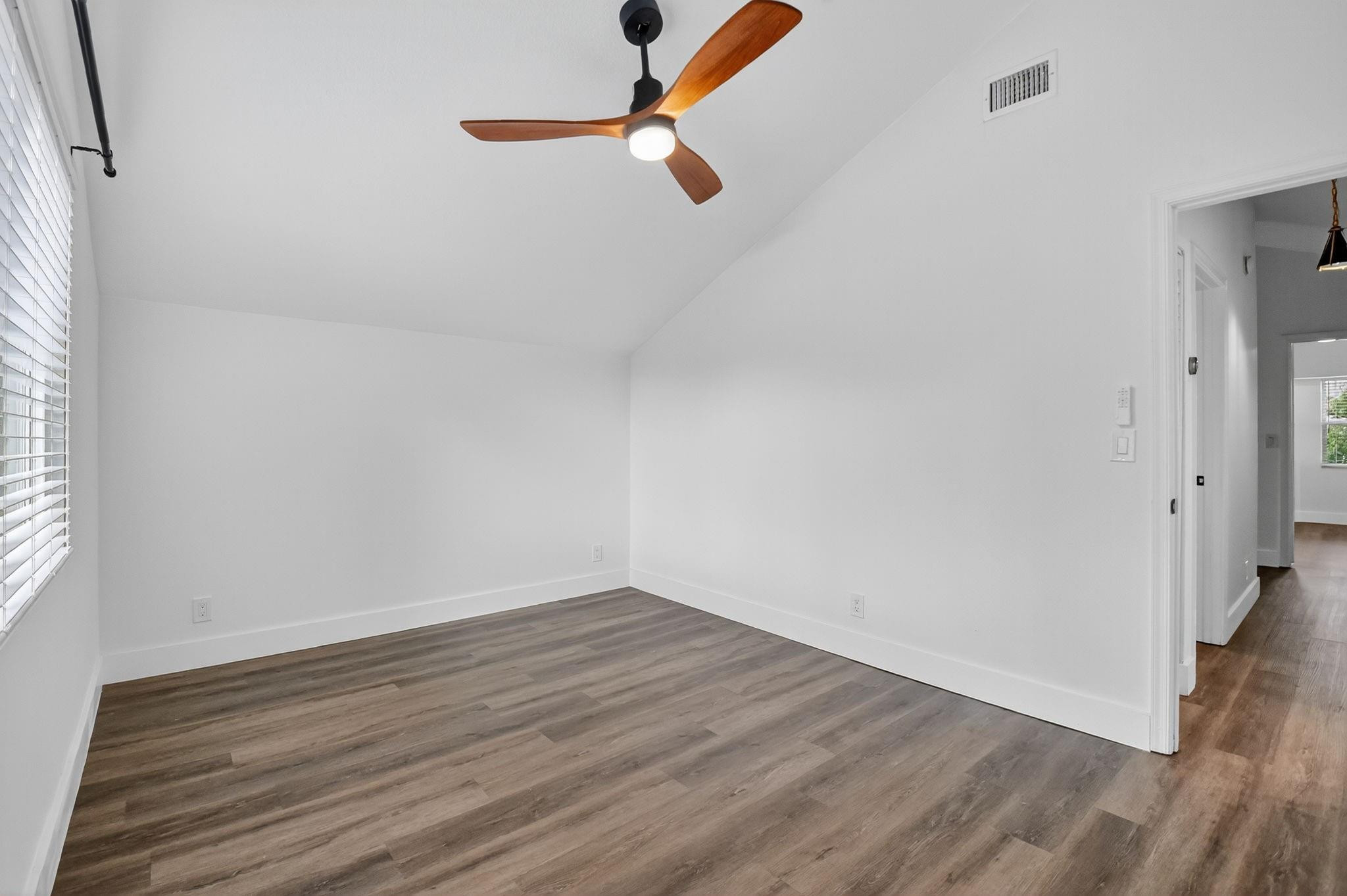 Empty room with gray-brown plank flooring, a wood-bladed ceiling fan, and a window with blinds.