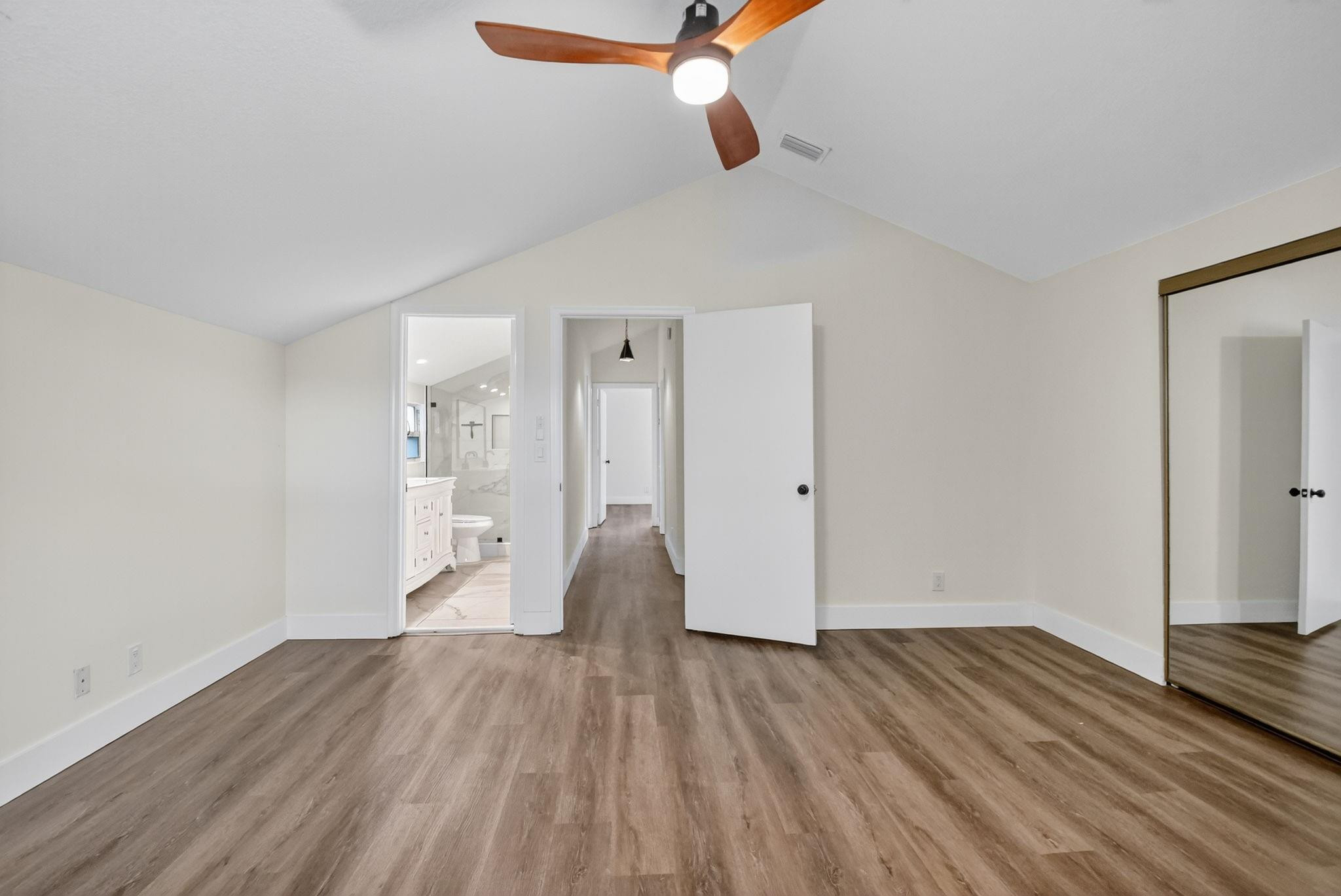 Vacant bedroom with vaulted ceiling, wood-look flooring, ceiling fan, and mirrored closet doors.