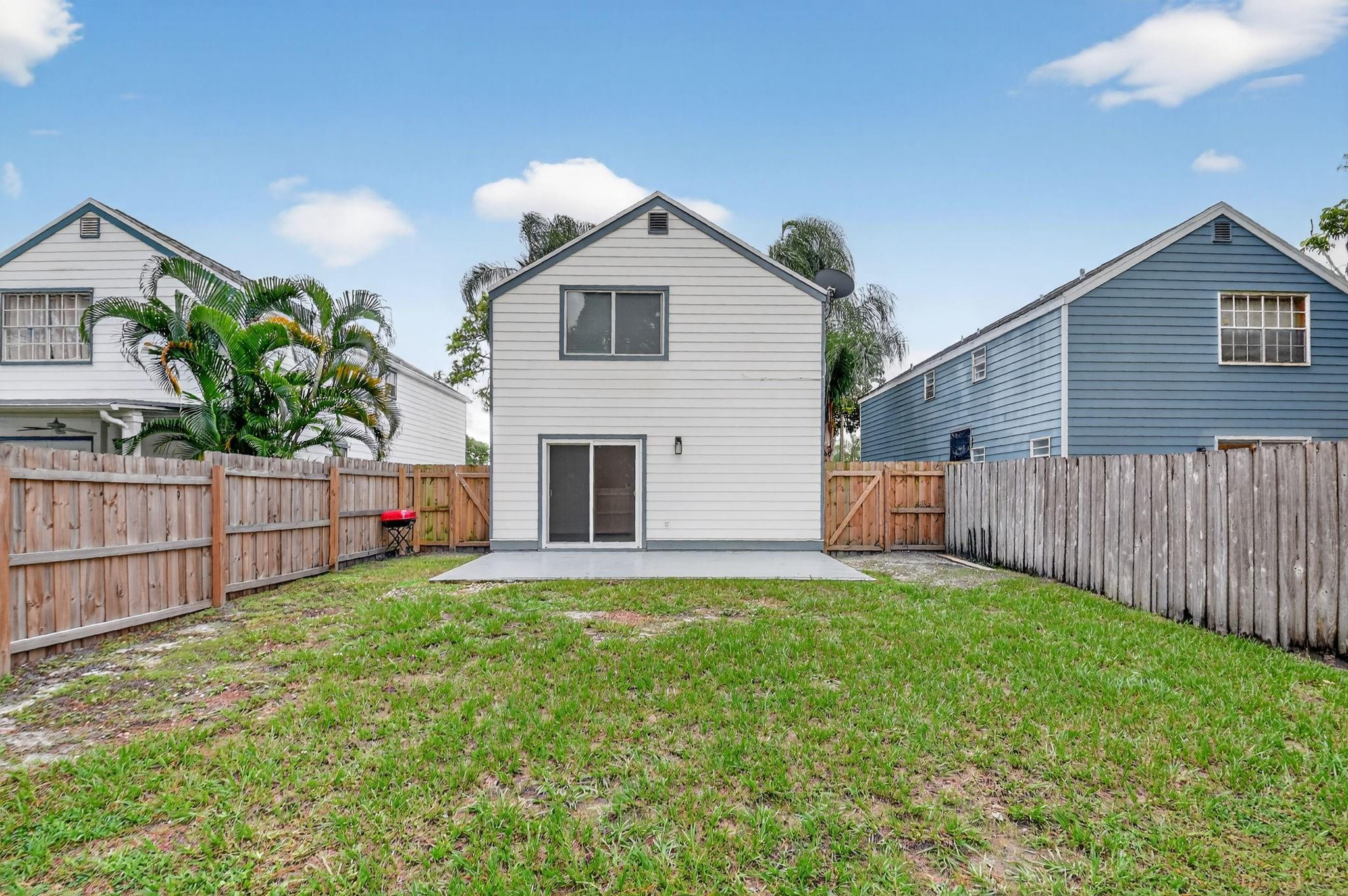 Two-story house rear with a fenced grassy yard, concrete patio, and neighboring homes.