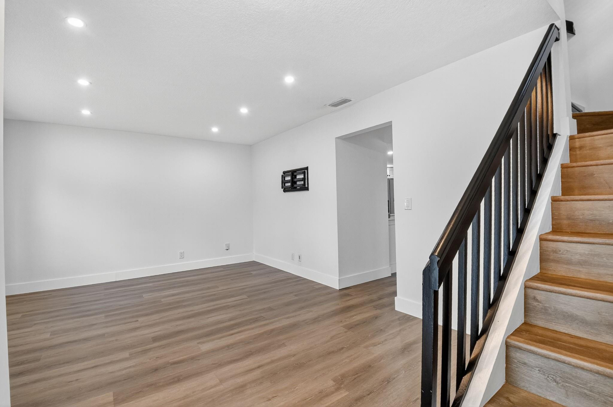 Empty room with plank flooring beside a staircase with wooden steps and a dark railing.