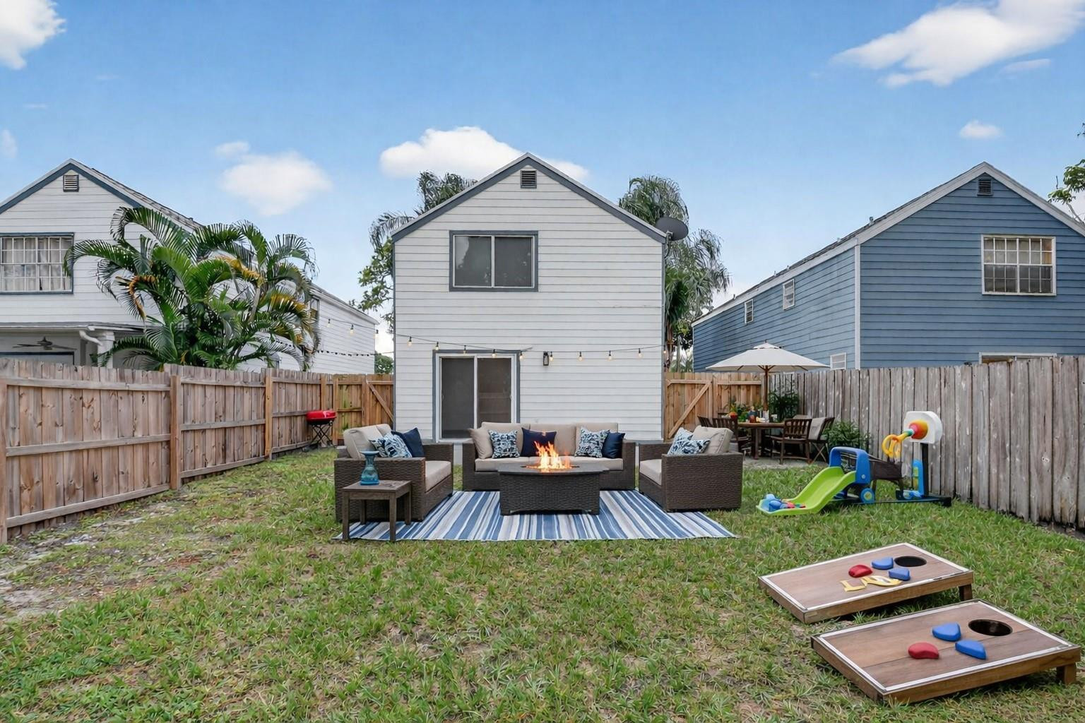Fenced backyard with patio seating around a fire pit and children's play equipment.