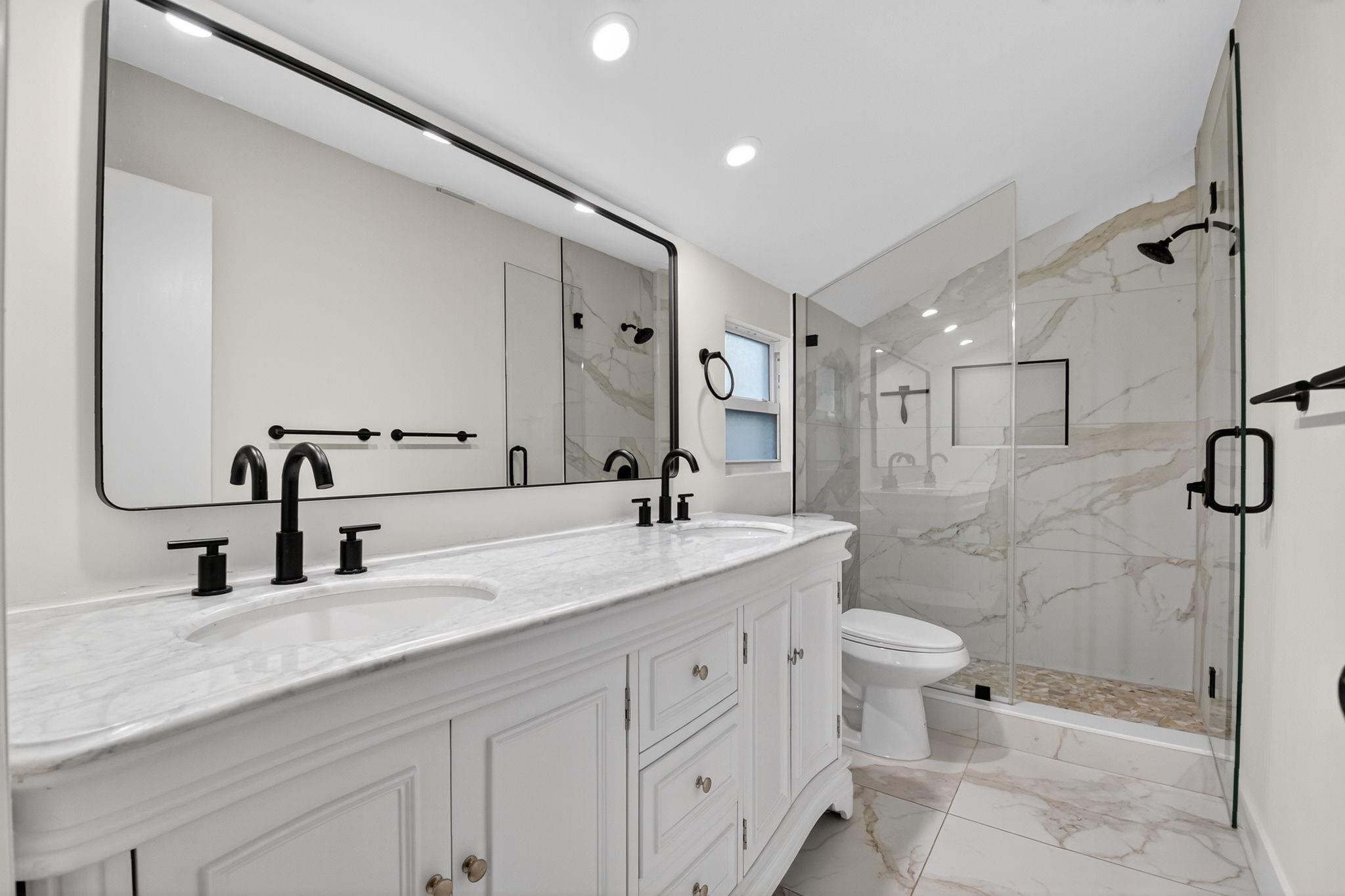 Bathroom with a white double vanity and glass shower lined with marble-look tile.
