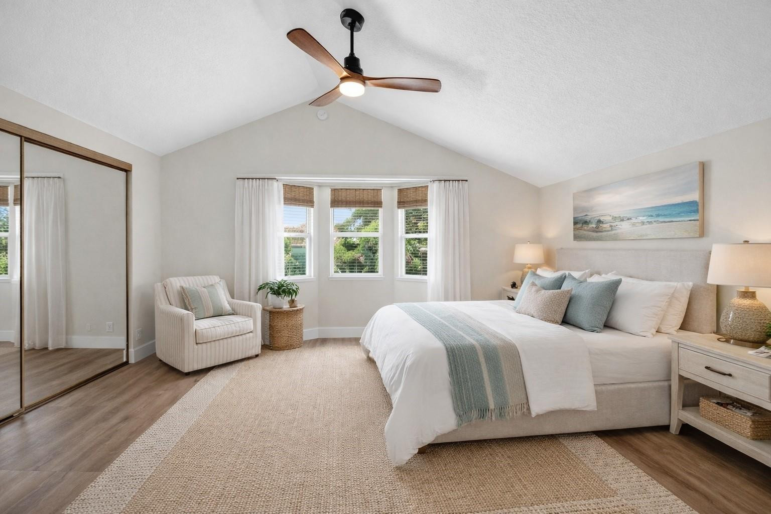 Bedroom with a king bed beneath a vaulted ceiling, wood-blade fan, and three curtained windows.