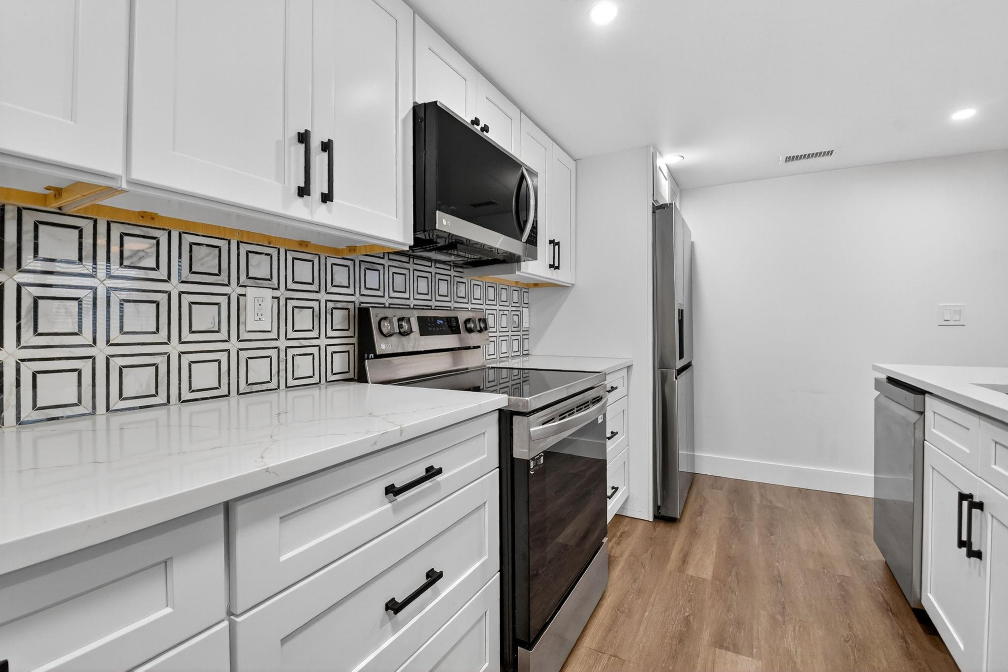Kitchen with white cabinets, stainless steel appliances, and a geometric black-and-white tile backsplash.