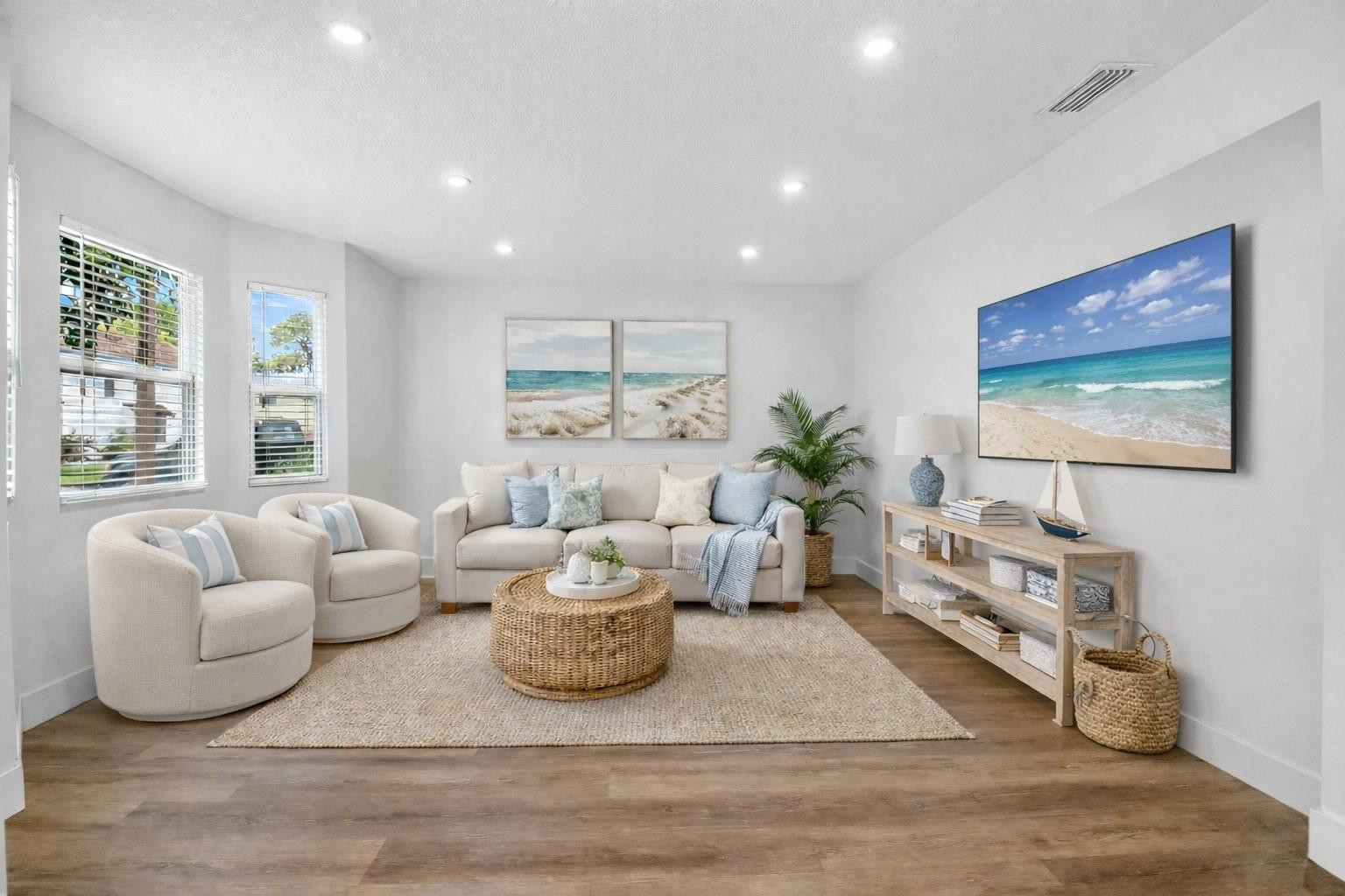 Staged living room with cream seating, a woven coffee table, and coastal beach artwork.