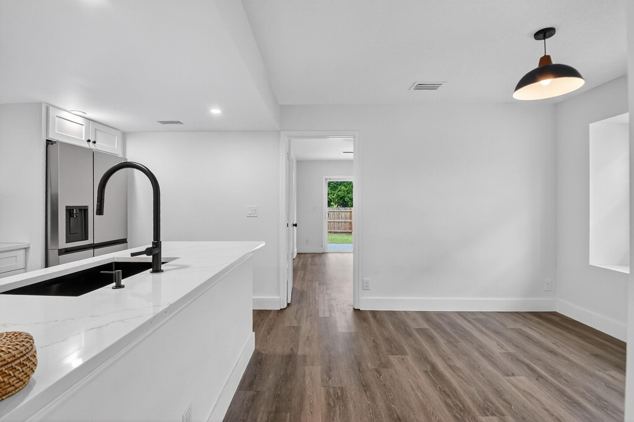 Vacant kitchen and dining area with a white peninsula, black faucet, stainless refrigerator, and brown wood-look flooring.