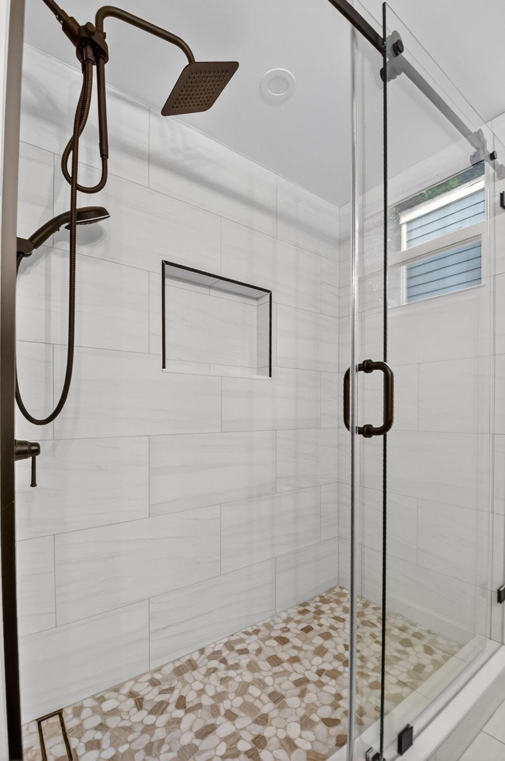 Walk-in shower with a pebble mosaic floor, glass enclosure, and dark bronze fixtures.