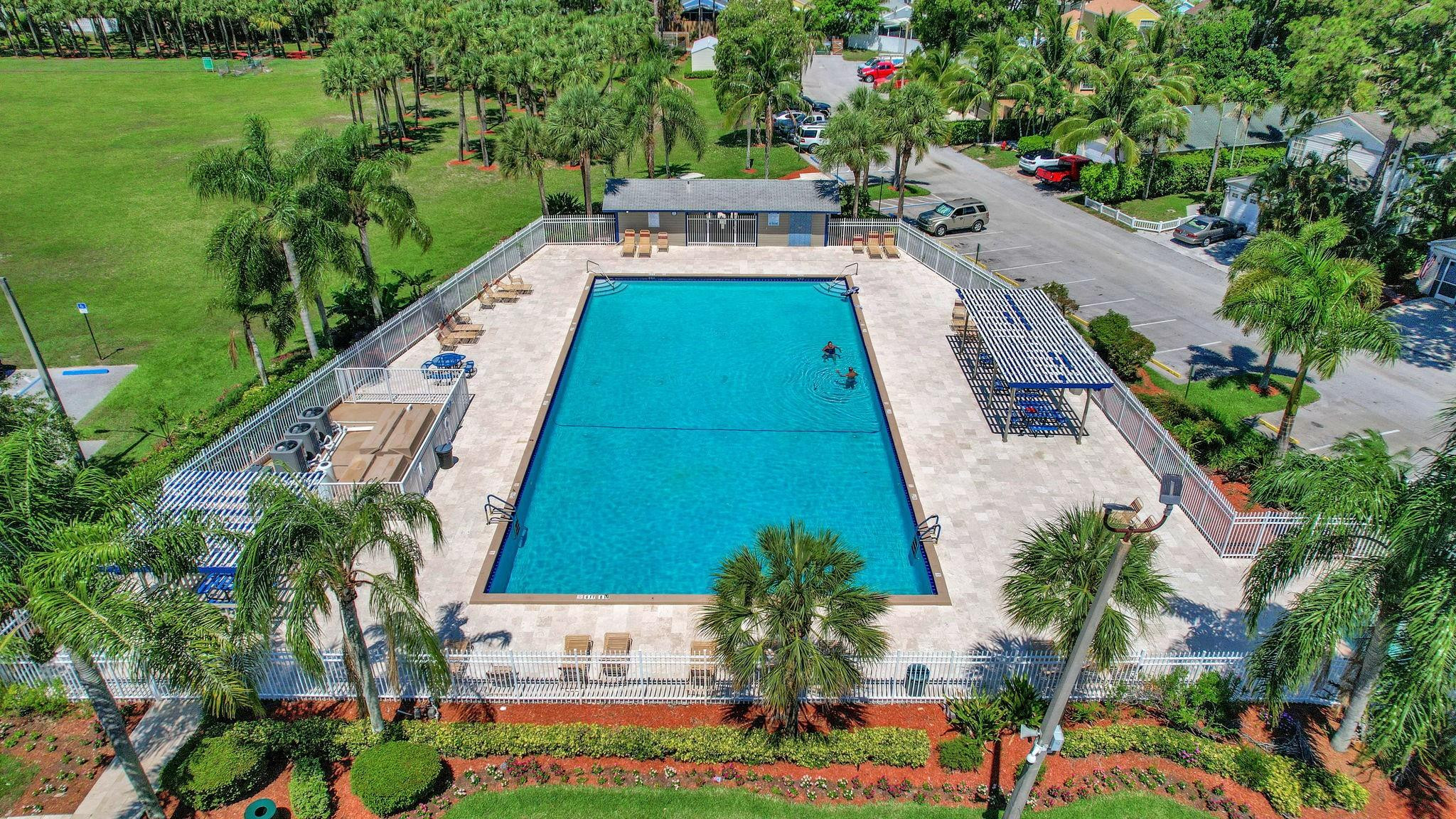 Aerial view of a community pool with a palm-lined deck, pergola, and two swimmers.