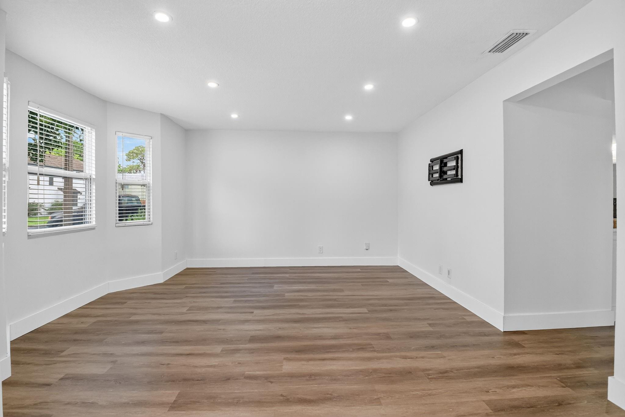 Vacant living room with wood-look flooring, two windows, and a wall-mounted TV bracket.