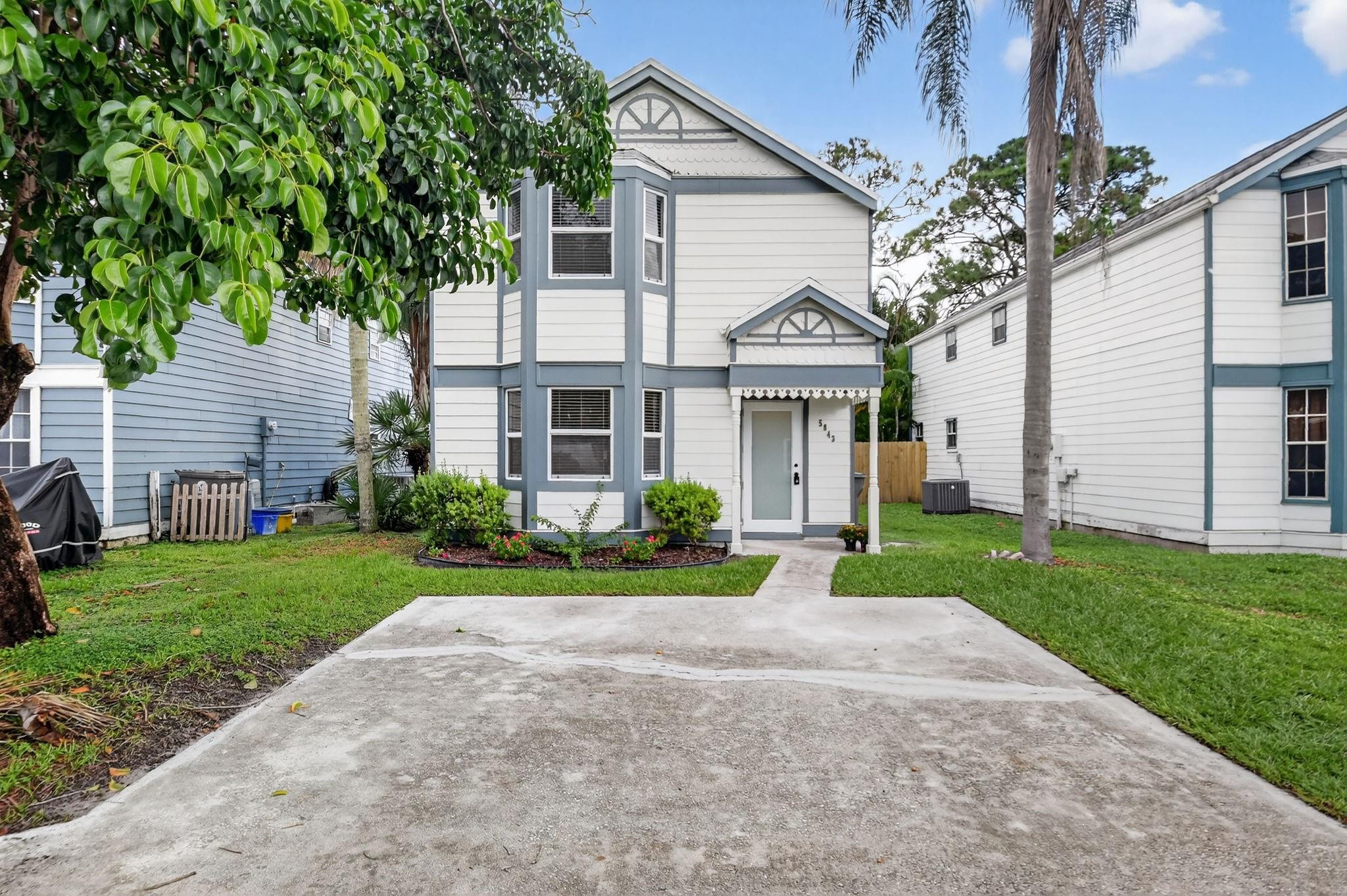 Two-story white home with blue-gray trim, a covered entry, landscaped garden, and wide concrete driveway.