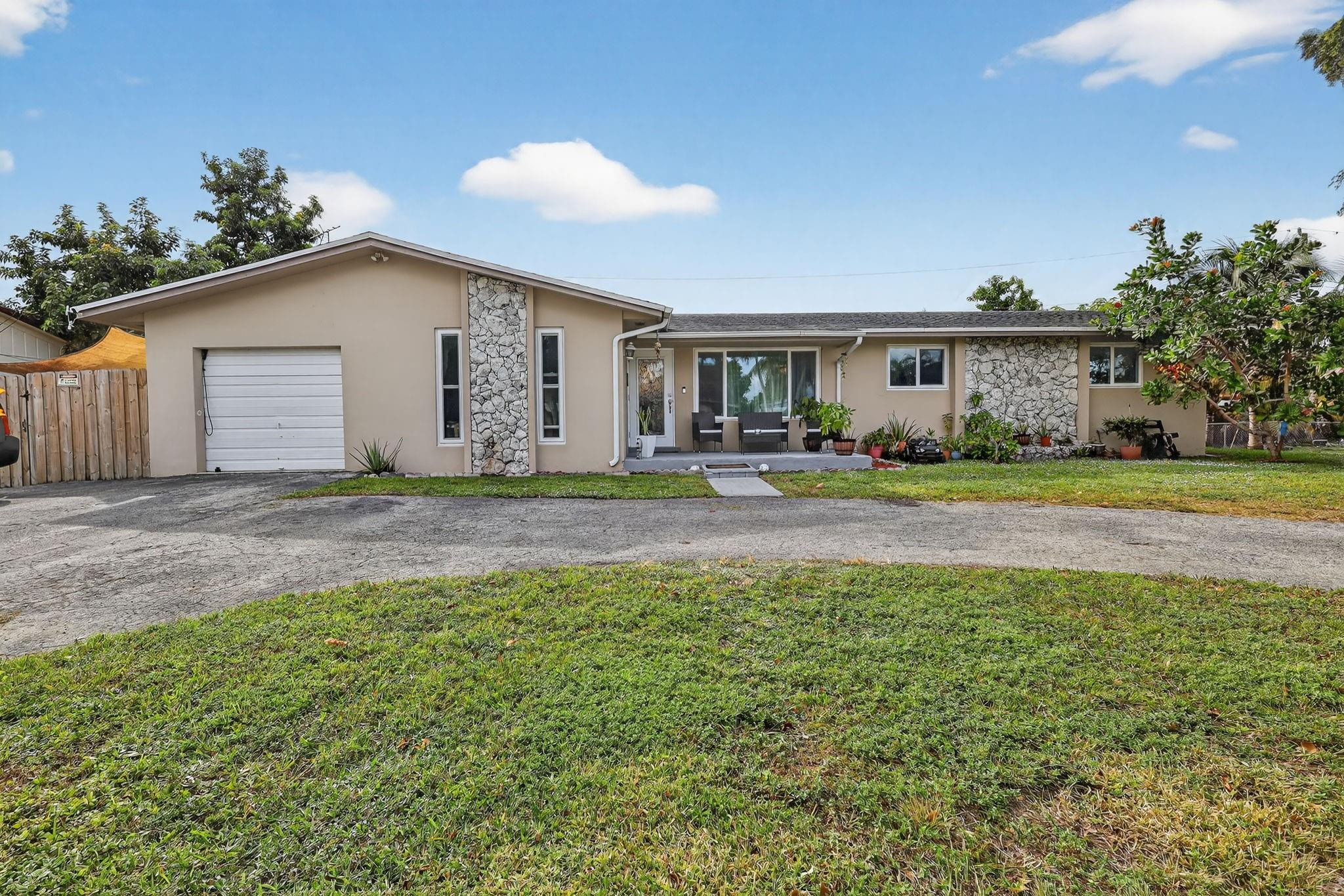 Single-story beige home with stone accents, an attached garage, and a small patio lined with plants.