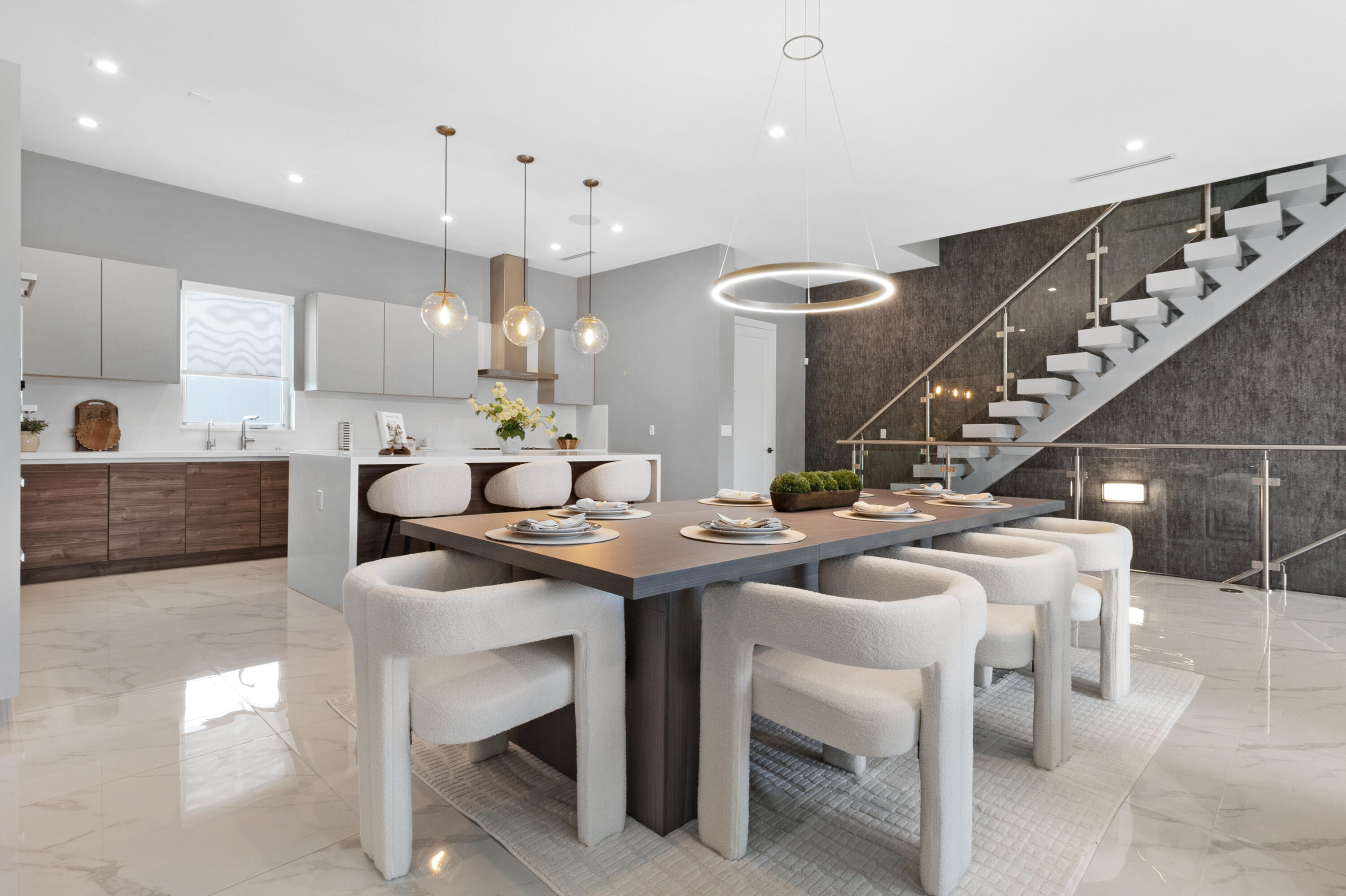 Modern dining area beside a white kitchen island, with a set table and glass-railed staircase.