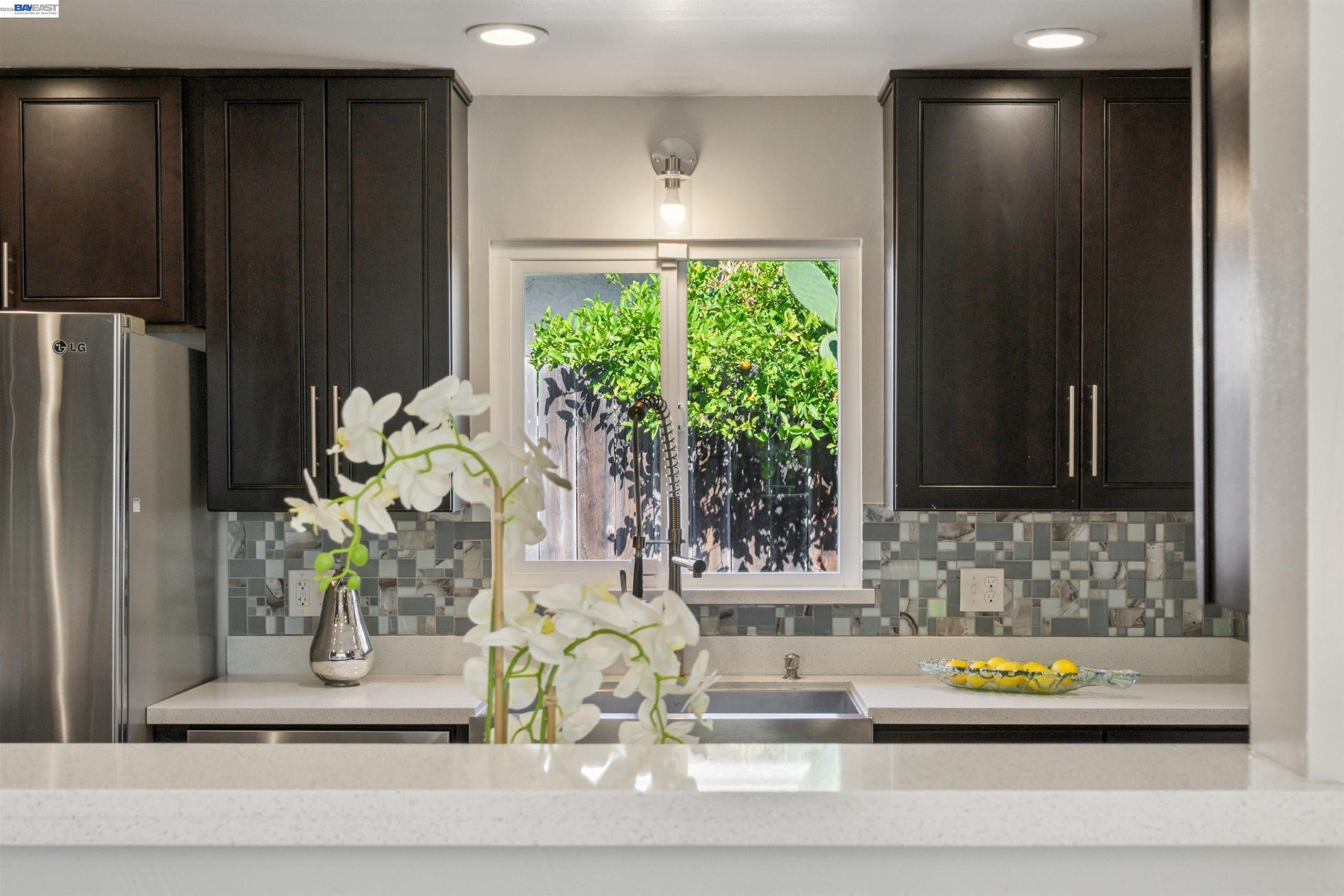 Kitchen with dark cabinets, mosaic tile backsplash, and a sink beneath a garden-facing window.