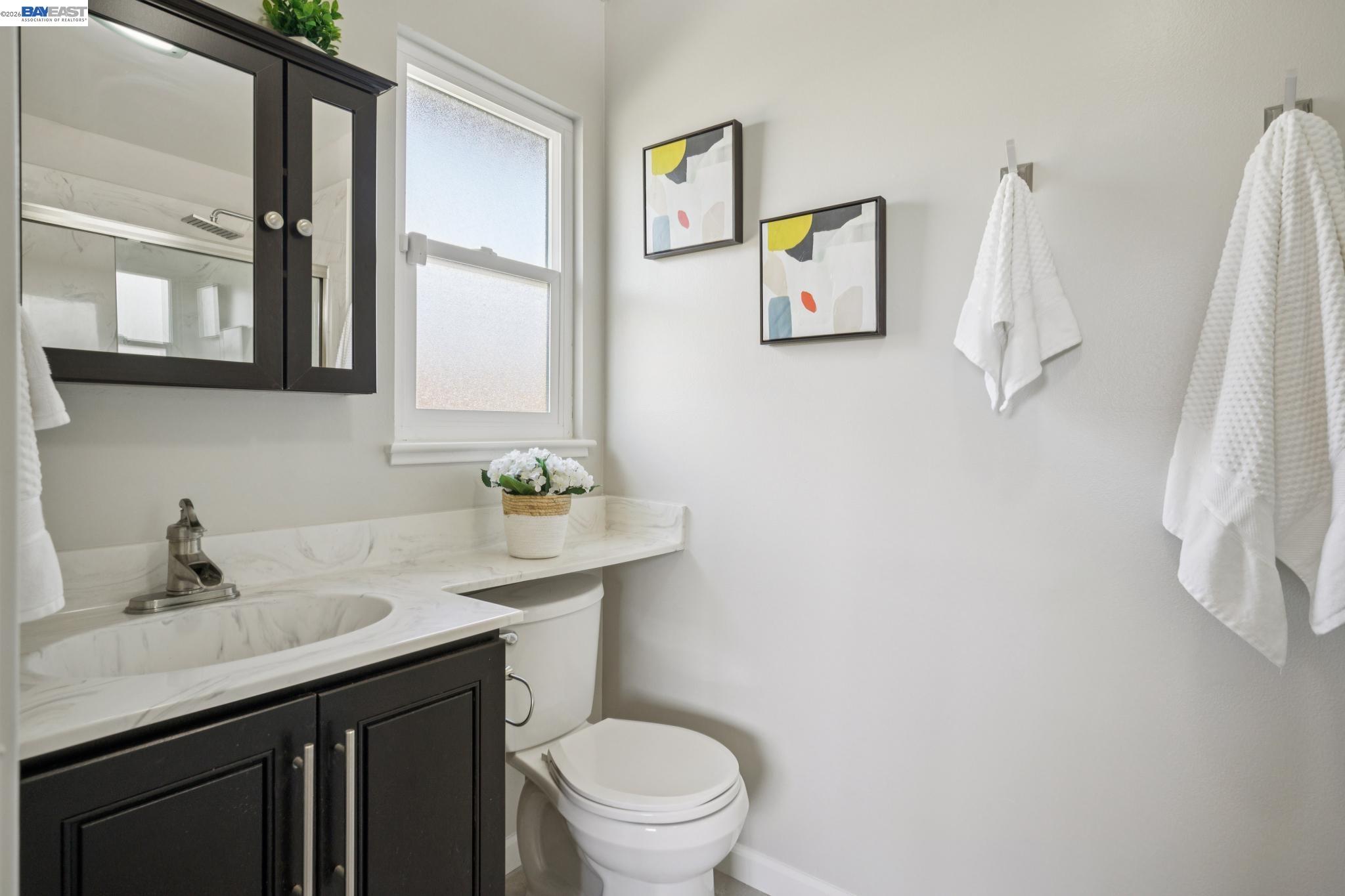 Bathroom with a marble-look vanity, dark cabinetry, frosted window, and white towels.