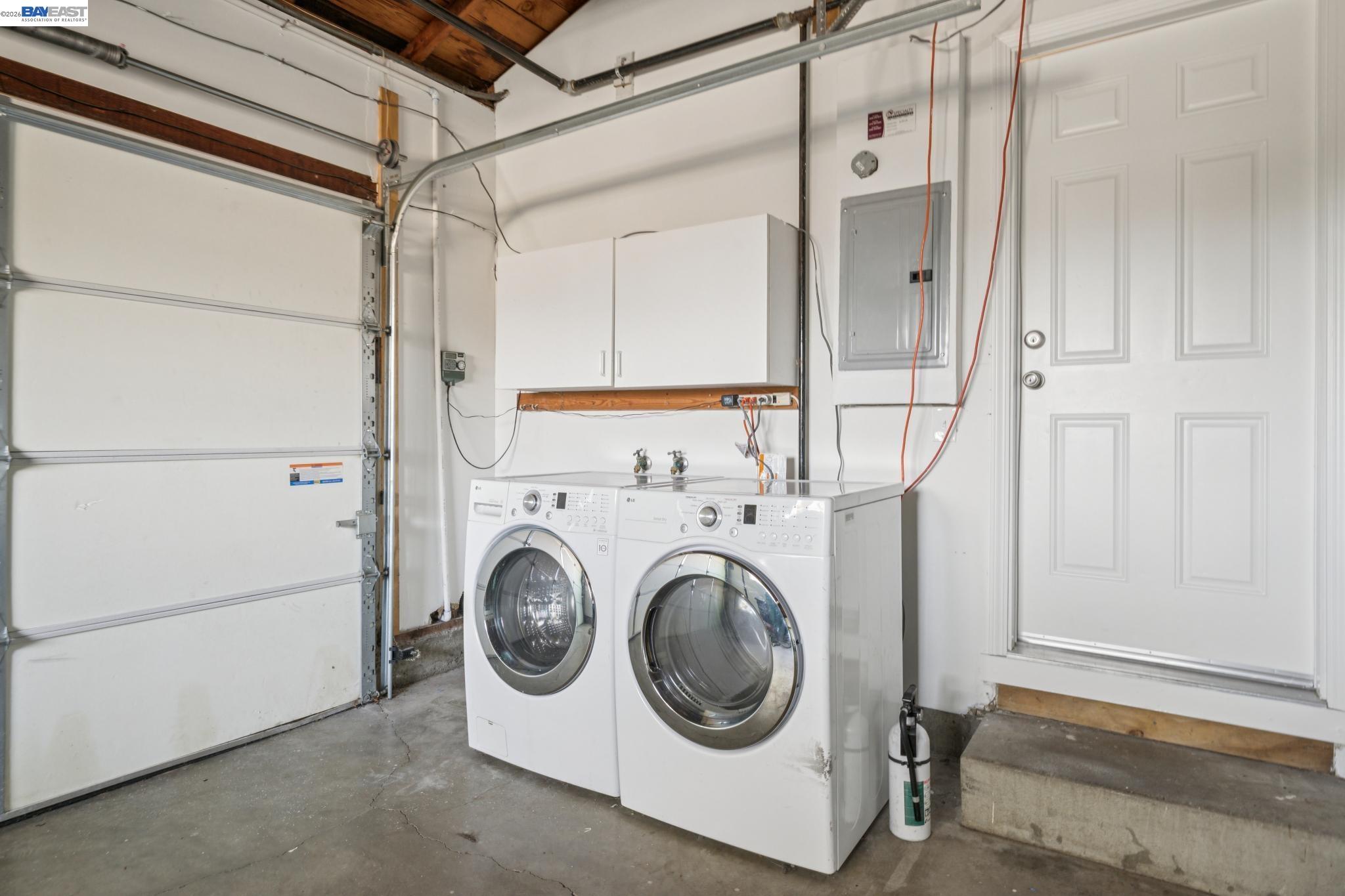 Garage laundry area with front-loading washer and dryer beneath white cabinets.