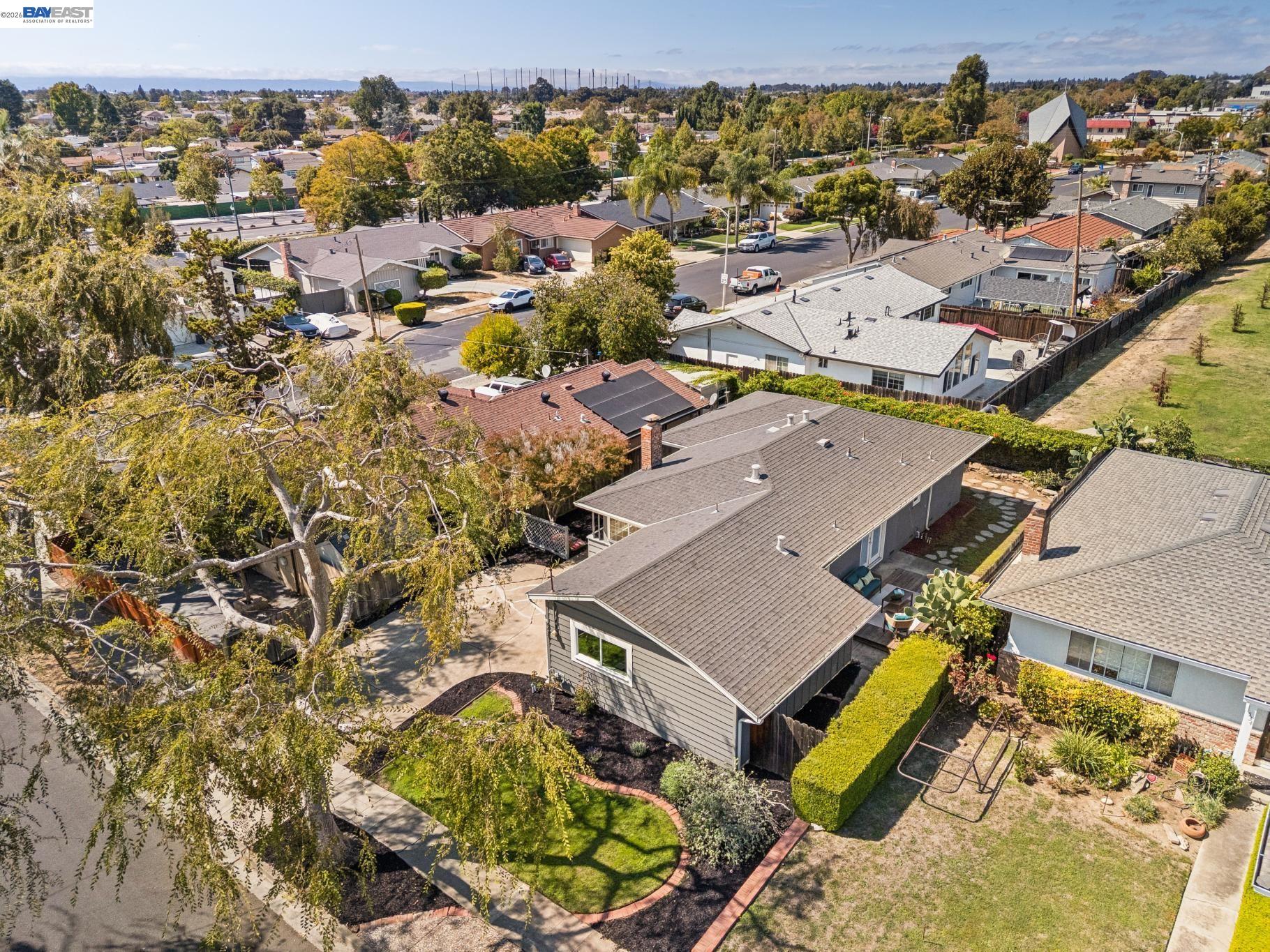 Aerial view of a gray single-story home with a curved landscaped front yard among neighboring houses.