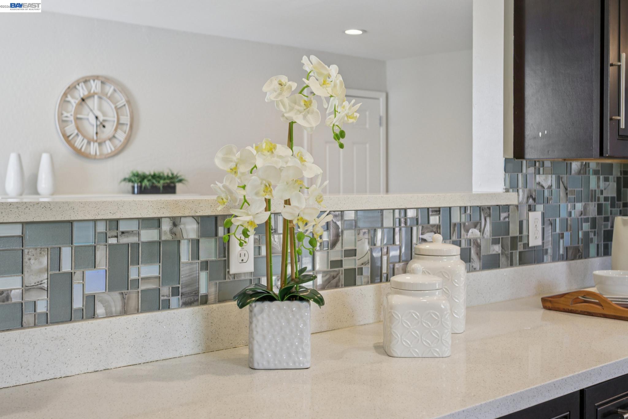 Kitchen counter with a blue-gray mosaic backsplash and white orchids.