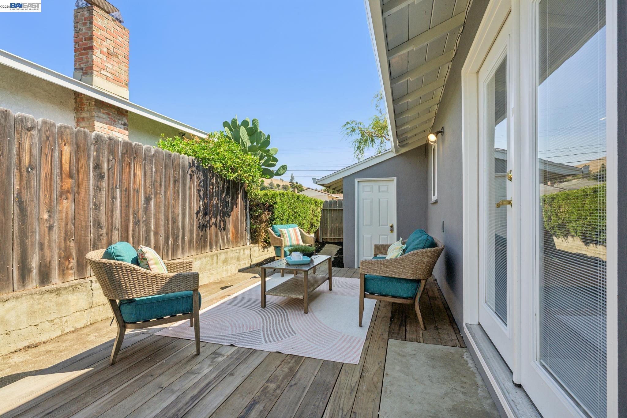 Furnished backyard patio with wicker seating, a striped rug and wooden deck beside sliding glass doors.