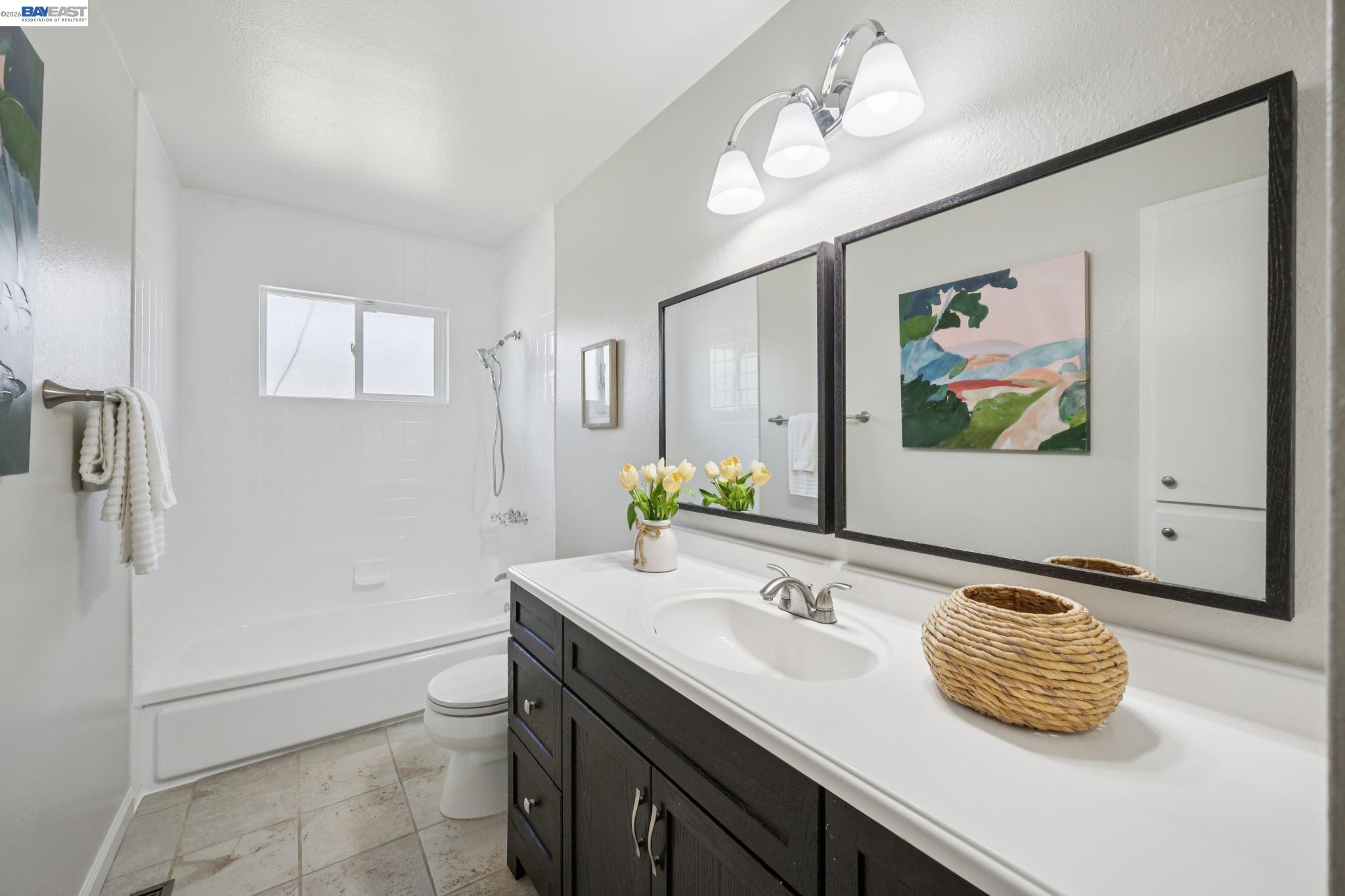 Bathroom with white tub and shower beside a dark vanity with large mirrors and yellow tulips.