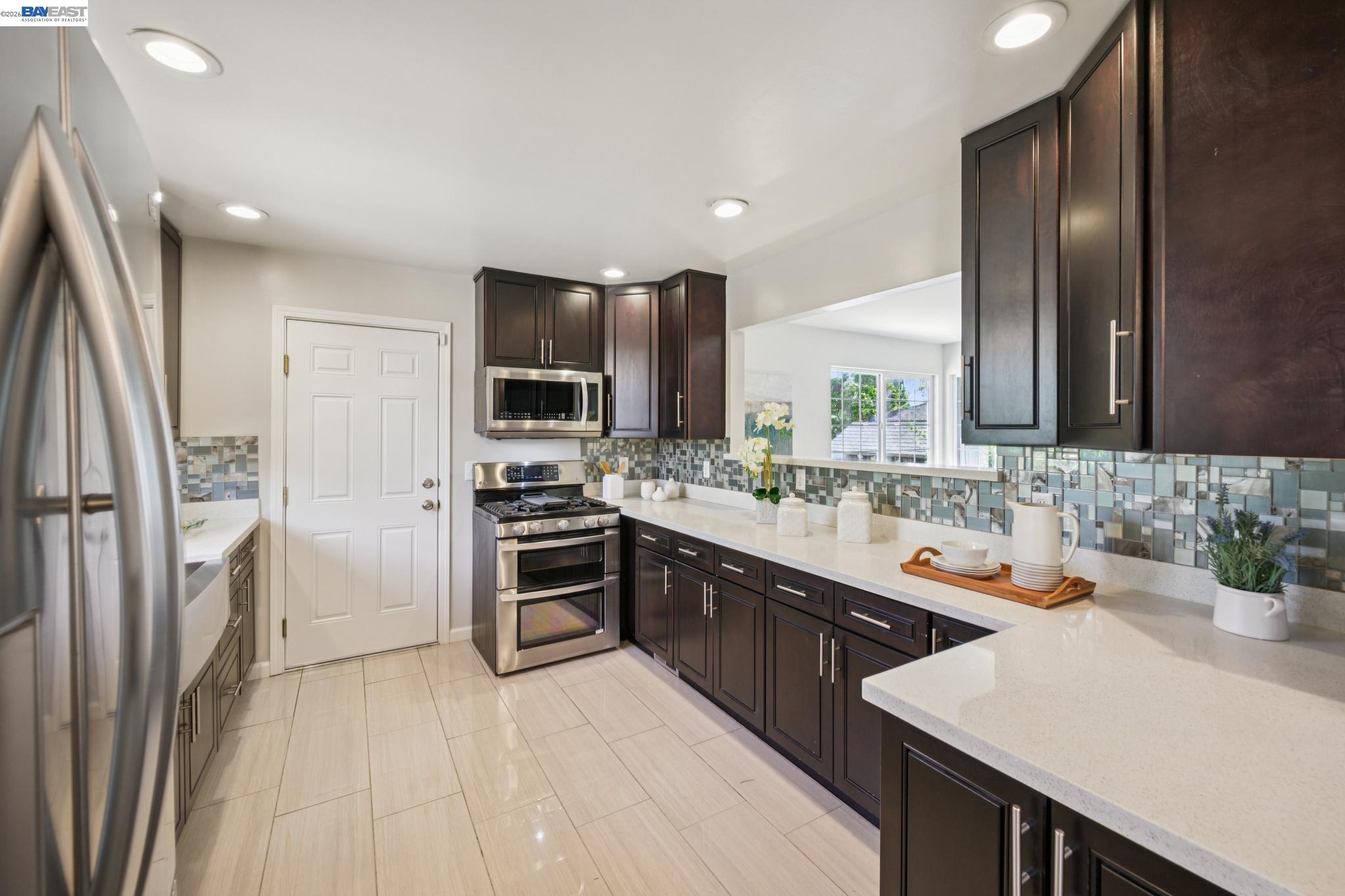Kitchen with dark cabinets, stainless steel appliances, and a blue-gray mosaic tile backsplash.