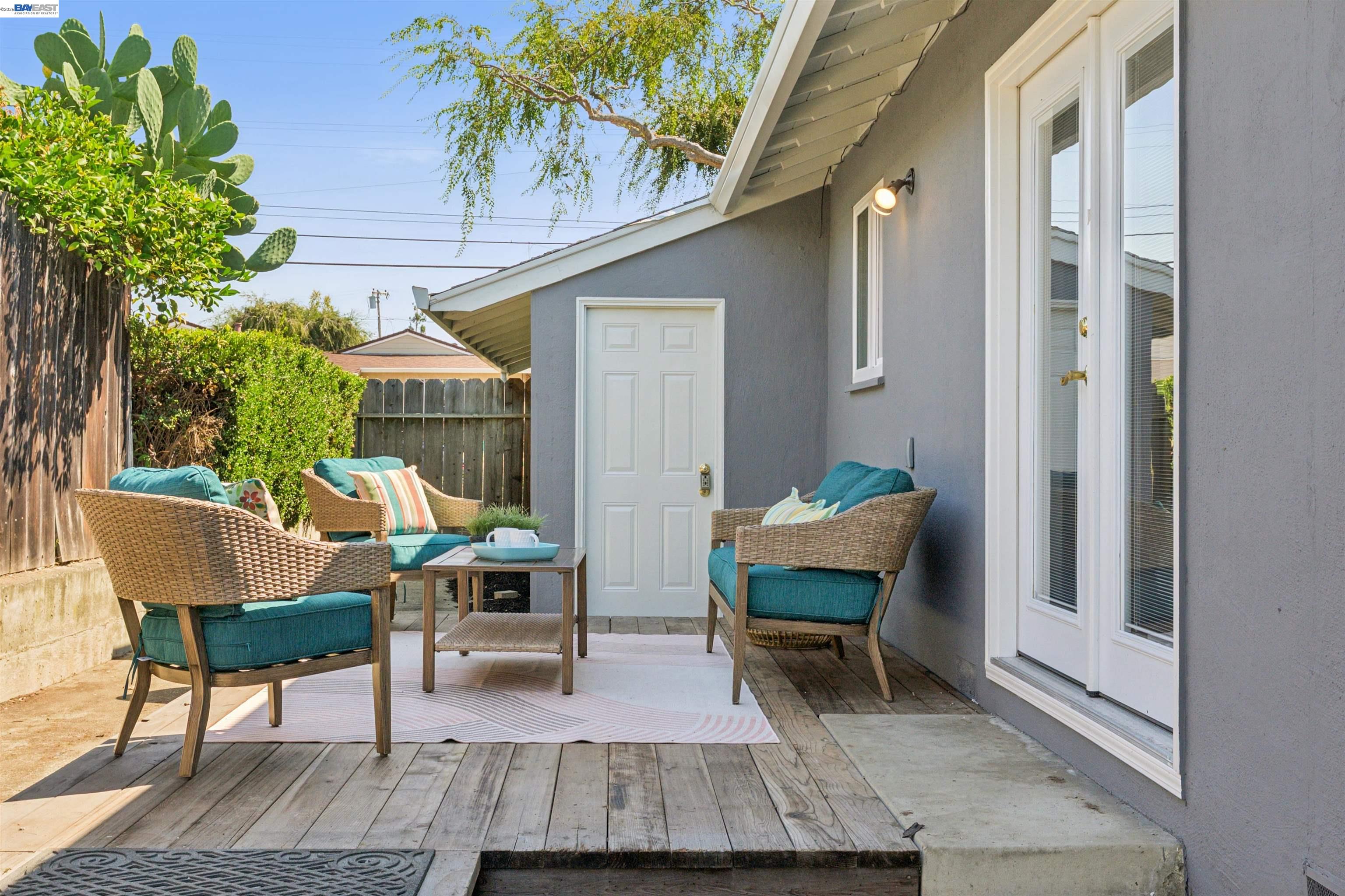 Furnished backyard patio with teal-cushioned wicker chairs, a wooden deck, and a large prickly pear cactus.