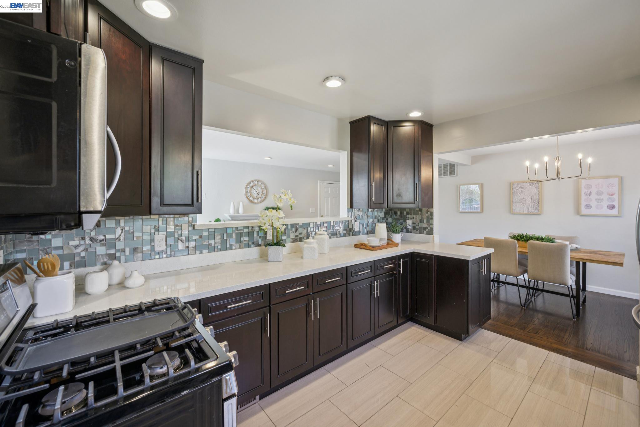 Kitchen with dark cabinets, mosaic tile backsplash, gas range, and an adjoining dining area.