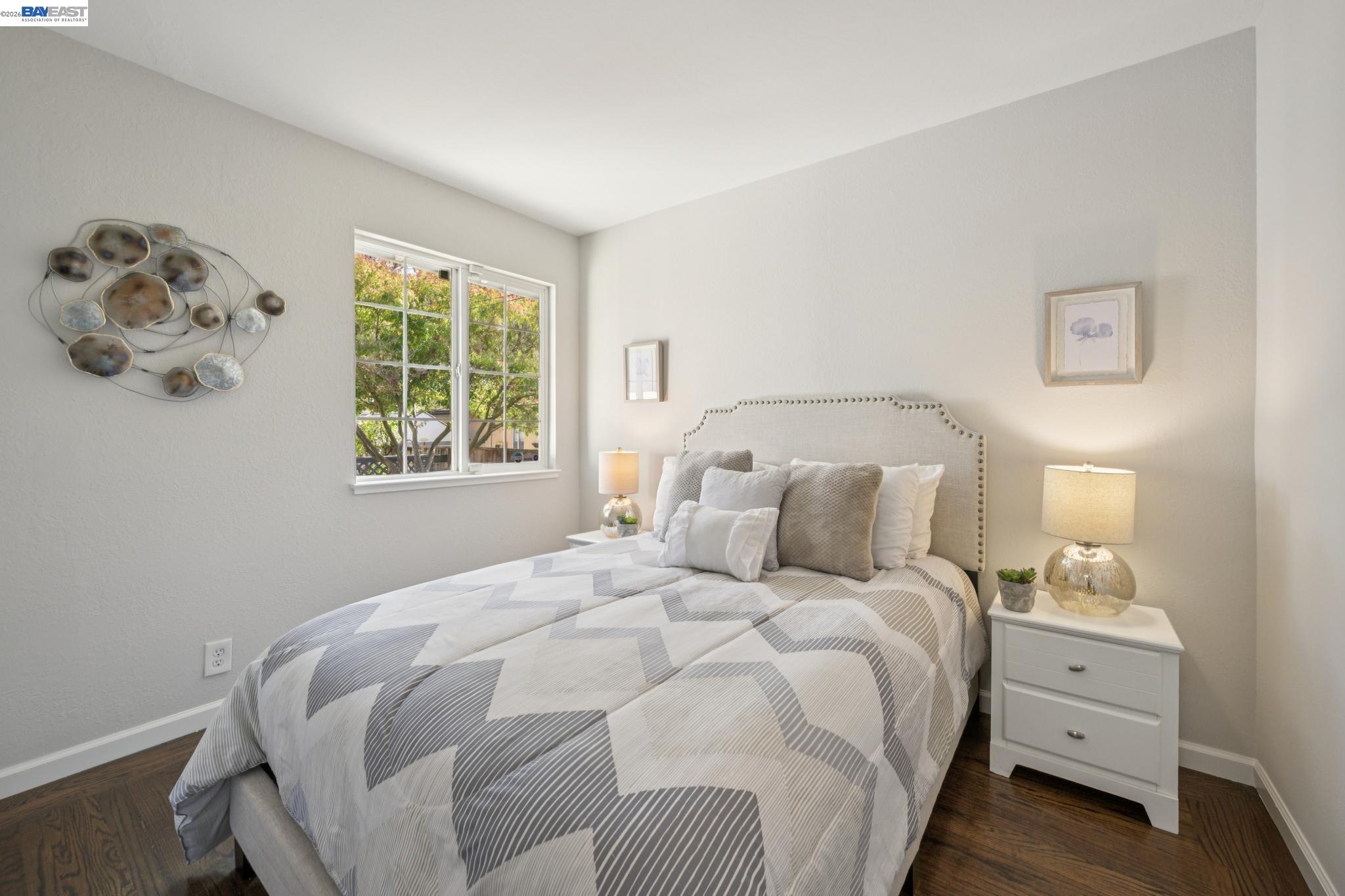 Staged bedroom with a gray-and-white geometric quilt and a window overlooking leafy trees.