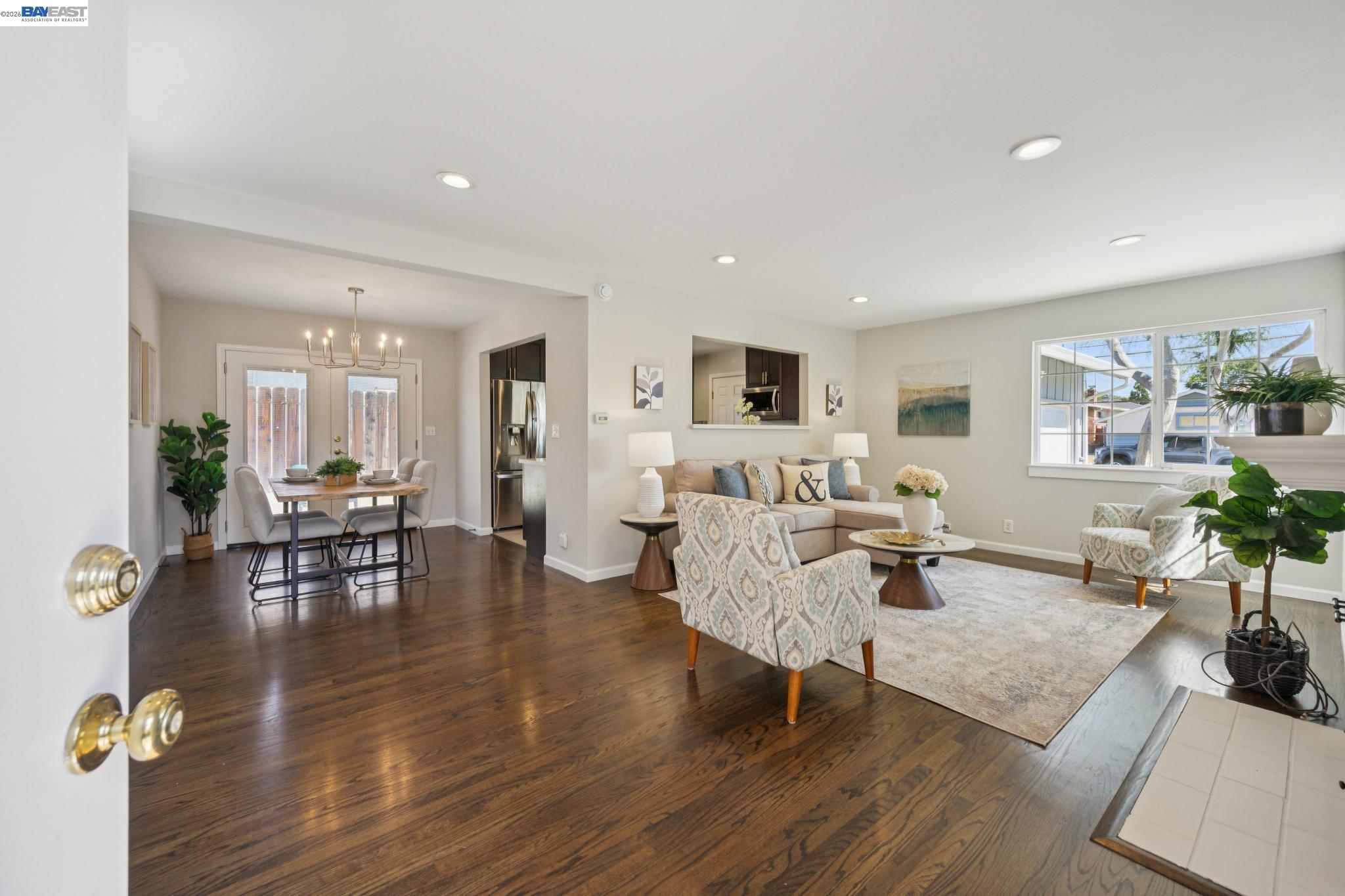 Open-plan living and dining room with dark hardwood floors, staged seating, and a kitchen with stainless steel appliances.