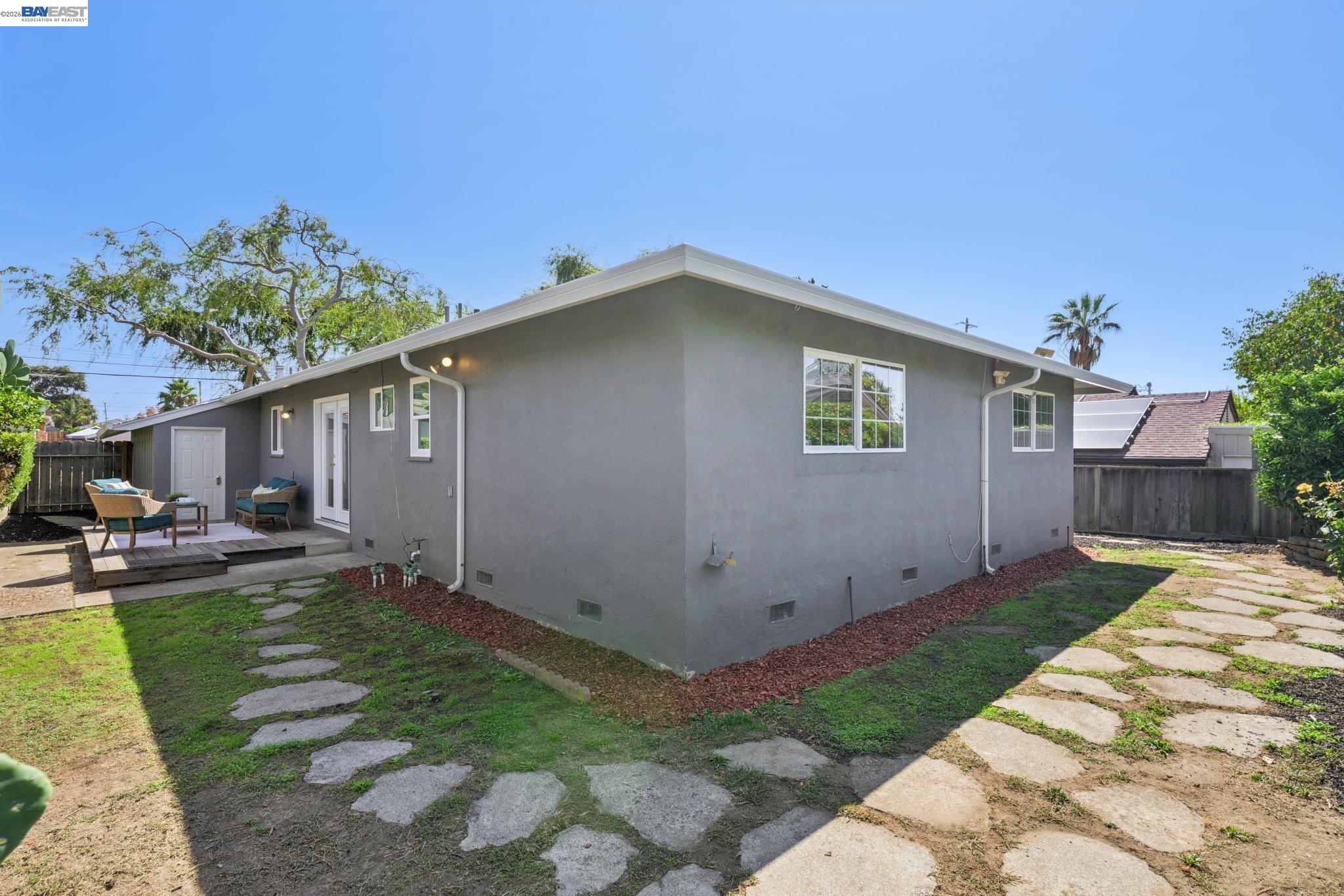 Gray single-story home's rear exterior, with a raised seating patio and stepping-stone paths across the backyard.