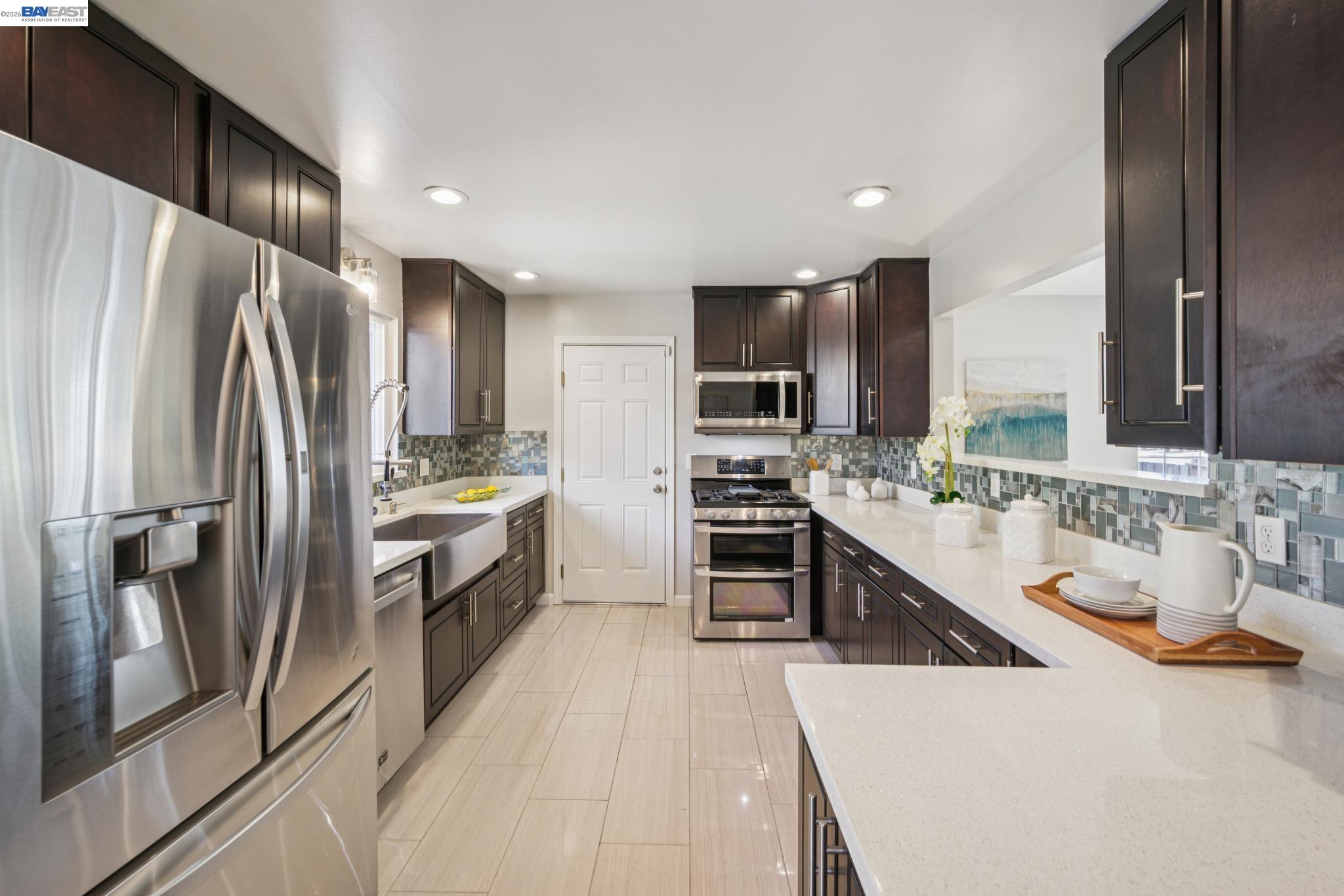 Kitchen with dark cabinets, stainless steel appliances, mosaic tile backsplash, and a white farmhouse sink.