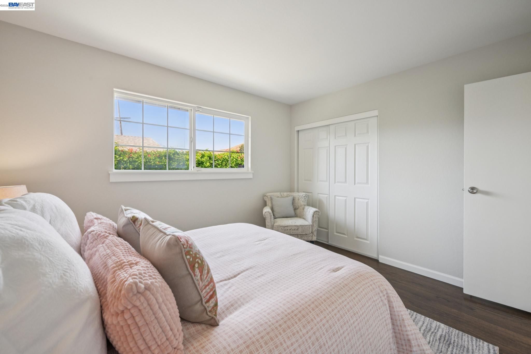 Bedroom with a pink-patterned bed, bright window, and white sliding closet doors.
