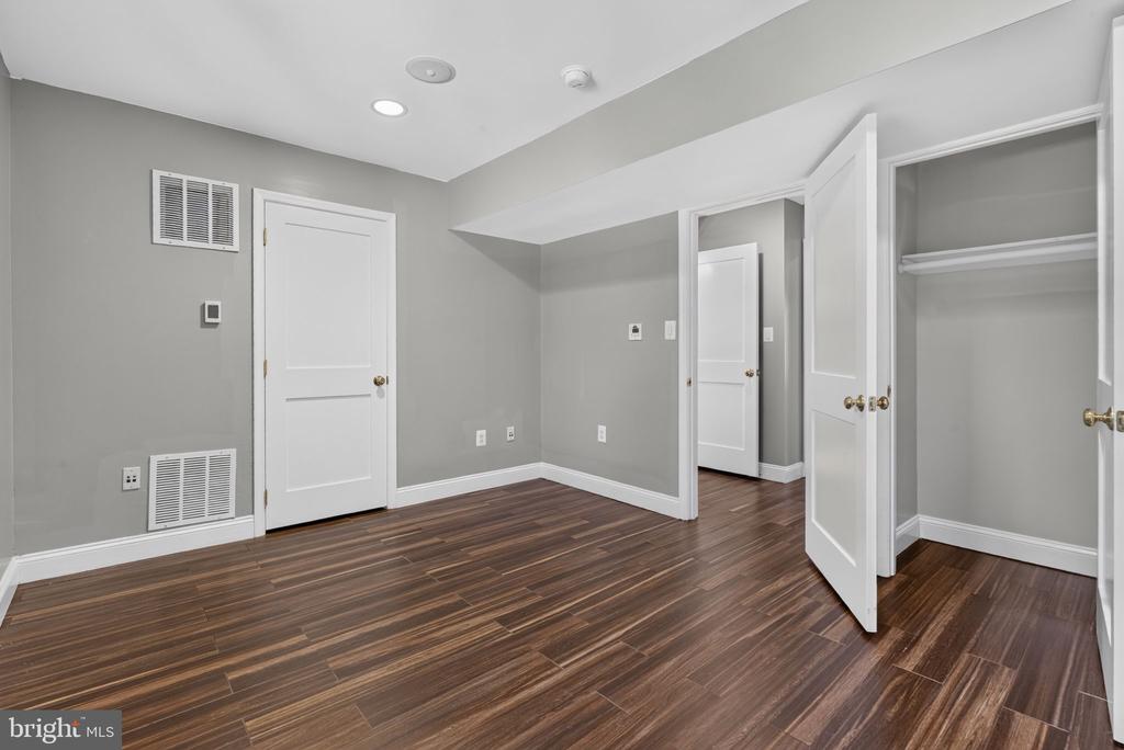 Empty bedroom with dark wood-look flooring, gray walls, and an open closet.