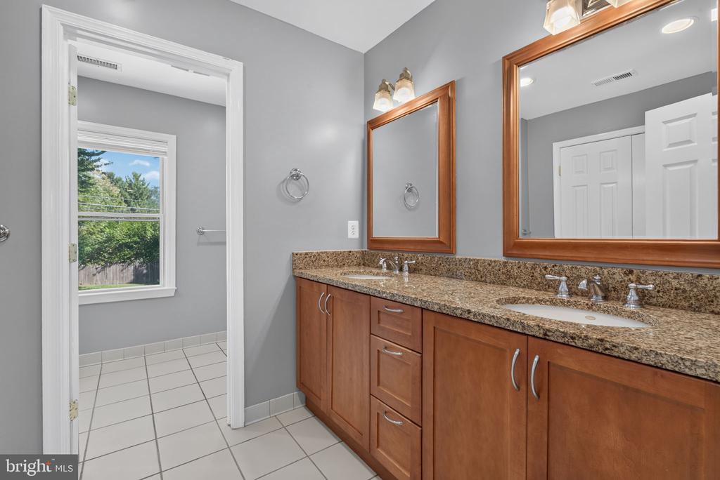 Bathroom with a double-sink wood vanity, granite countertop, framed mirrors, and an adjoining window.
