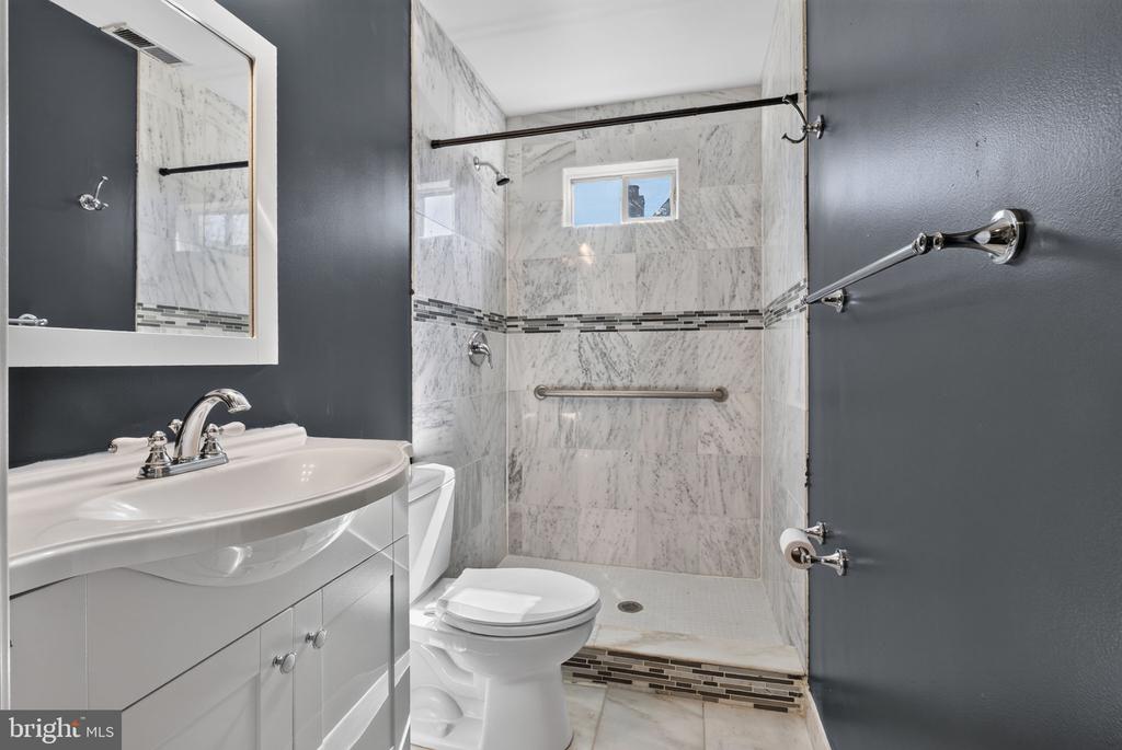 Bathroom with a marble-look tiled shower, mosaic accent band, white vanity, and toilet.