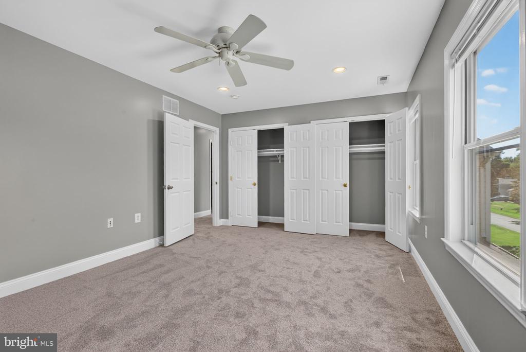 Empty bedroom with beige carpet, a ceiling fan, and several open closets.