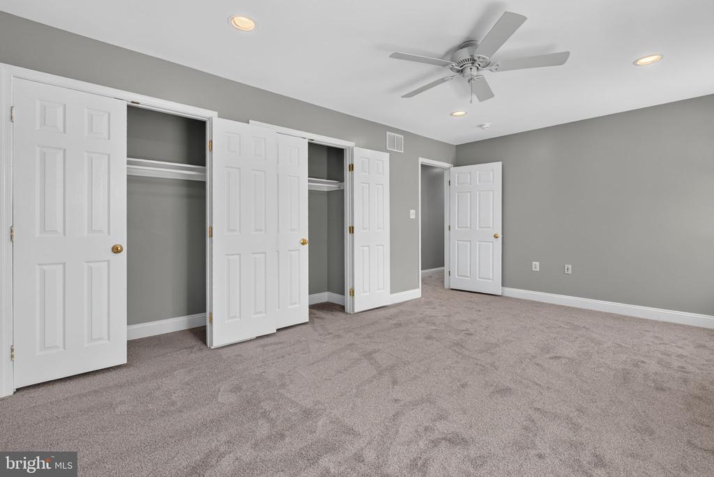 Vacant bedroom with beige carpet, two closets, and a ceiling fan.