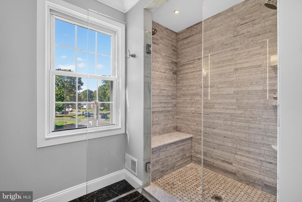 Bathroom with a glass-enclosed stone-tile shower, built-in bench, and large window.