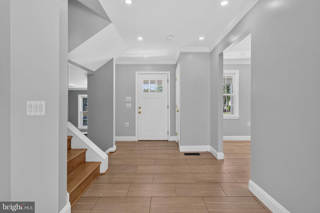 Entry foyer with wood-toned tile flooring, a white front door, and a staircase.
