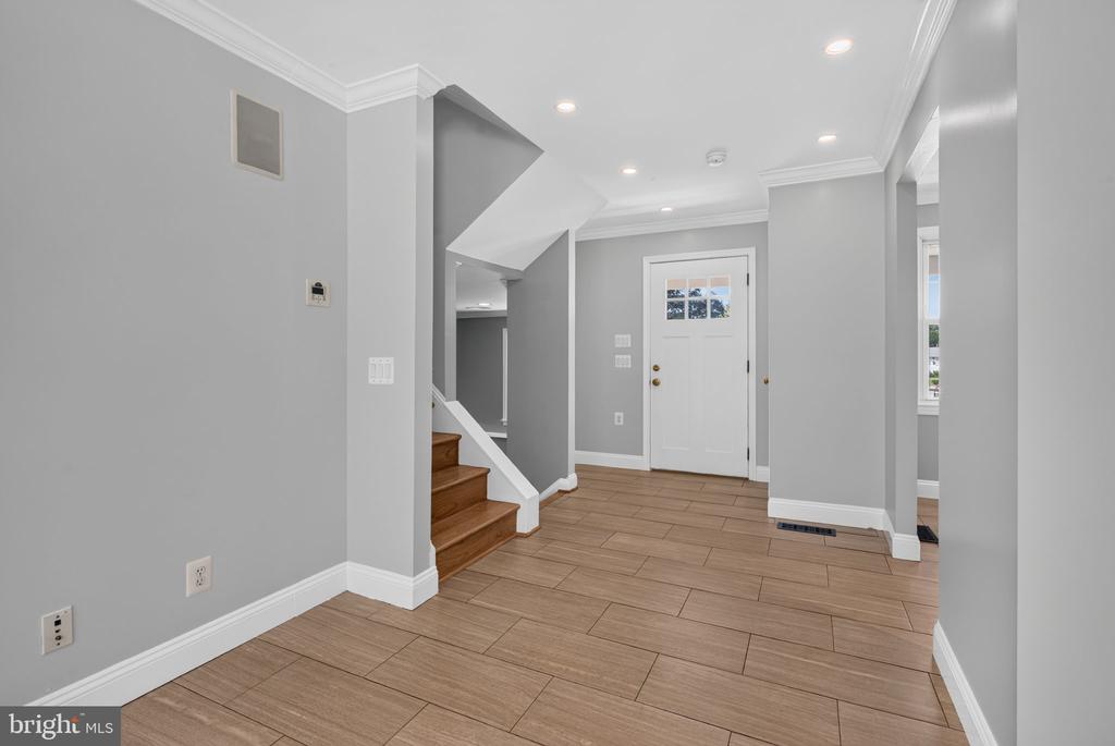 Entry foyer with wood-look tile flooring, staircase, and white front door.
