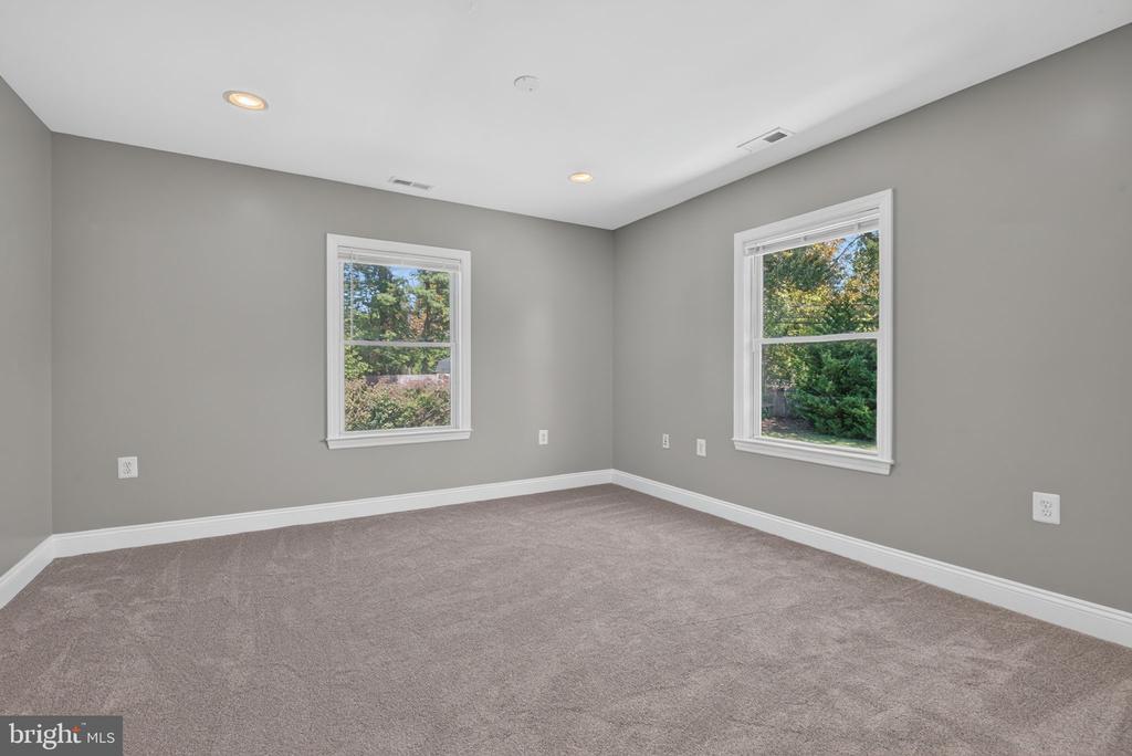 Empty carpeted room with gray walls and two windows overlooking greenery.