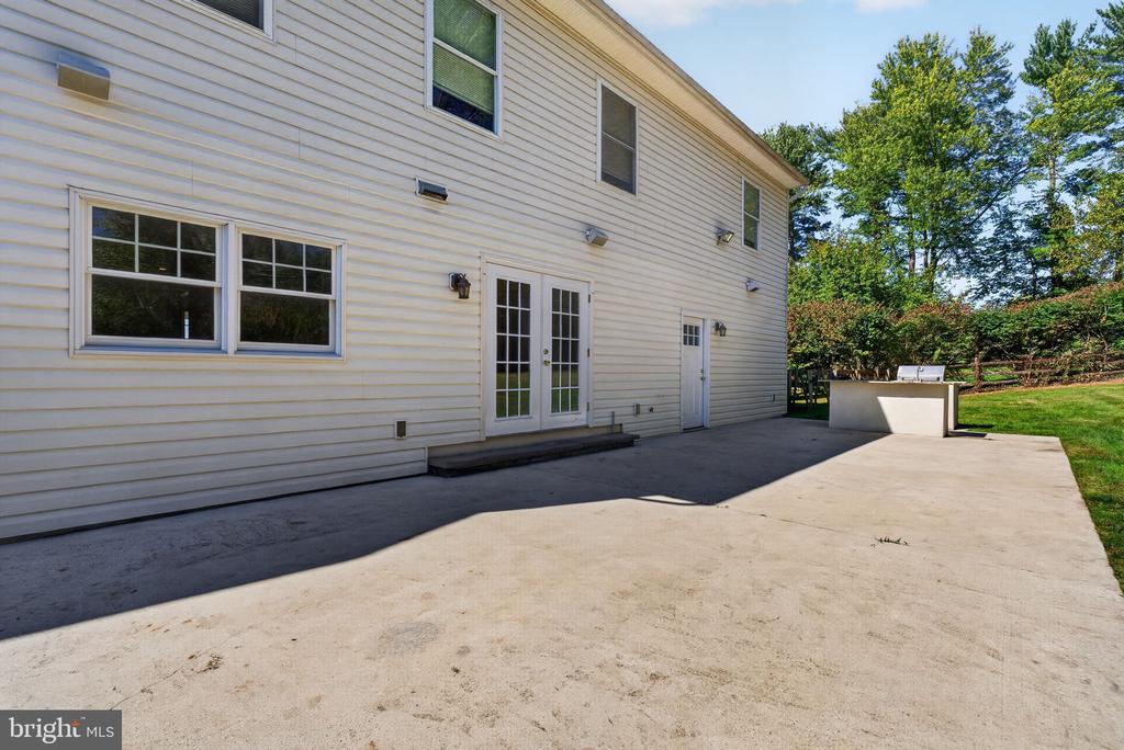 Two-story house beside a broad concrete patio with French doors and a built-in outdoor counter.