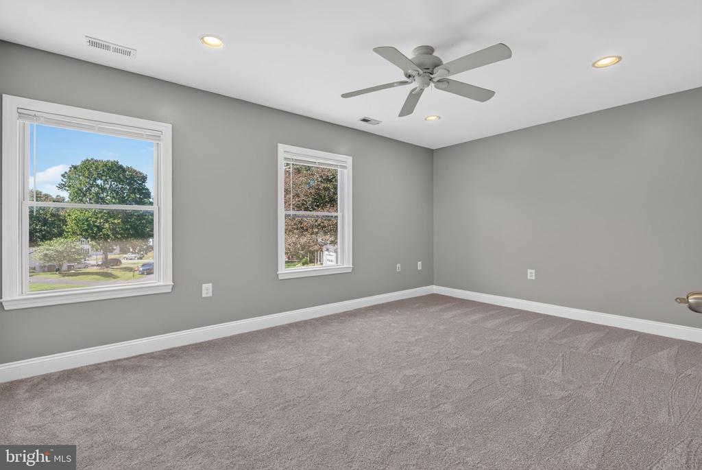 Empty bedroom with gray carpet, two windows, and a ceiling fan.